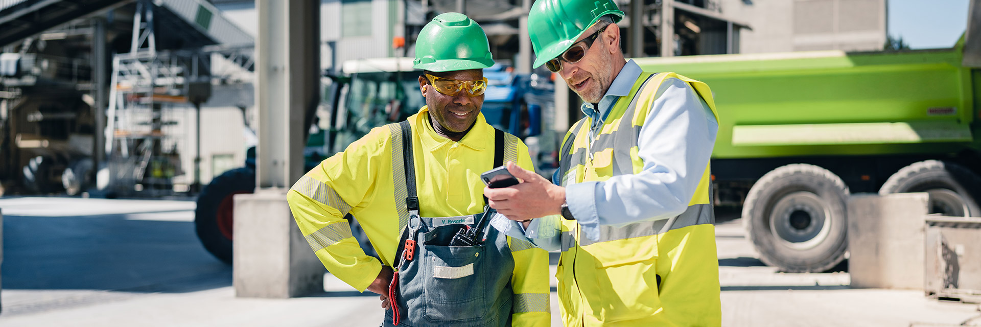Ein Bauarbeiter in gelber Weste zeigt seinem Kollegen etwas auf seinem Handy
