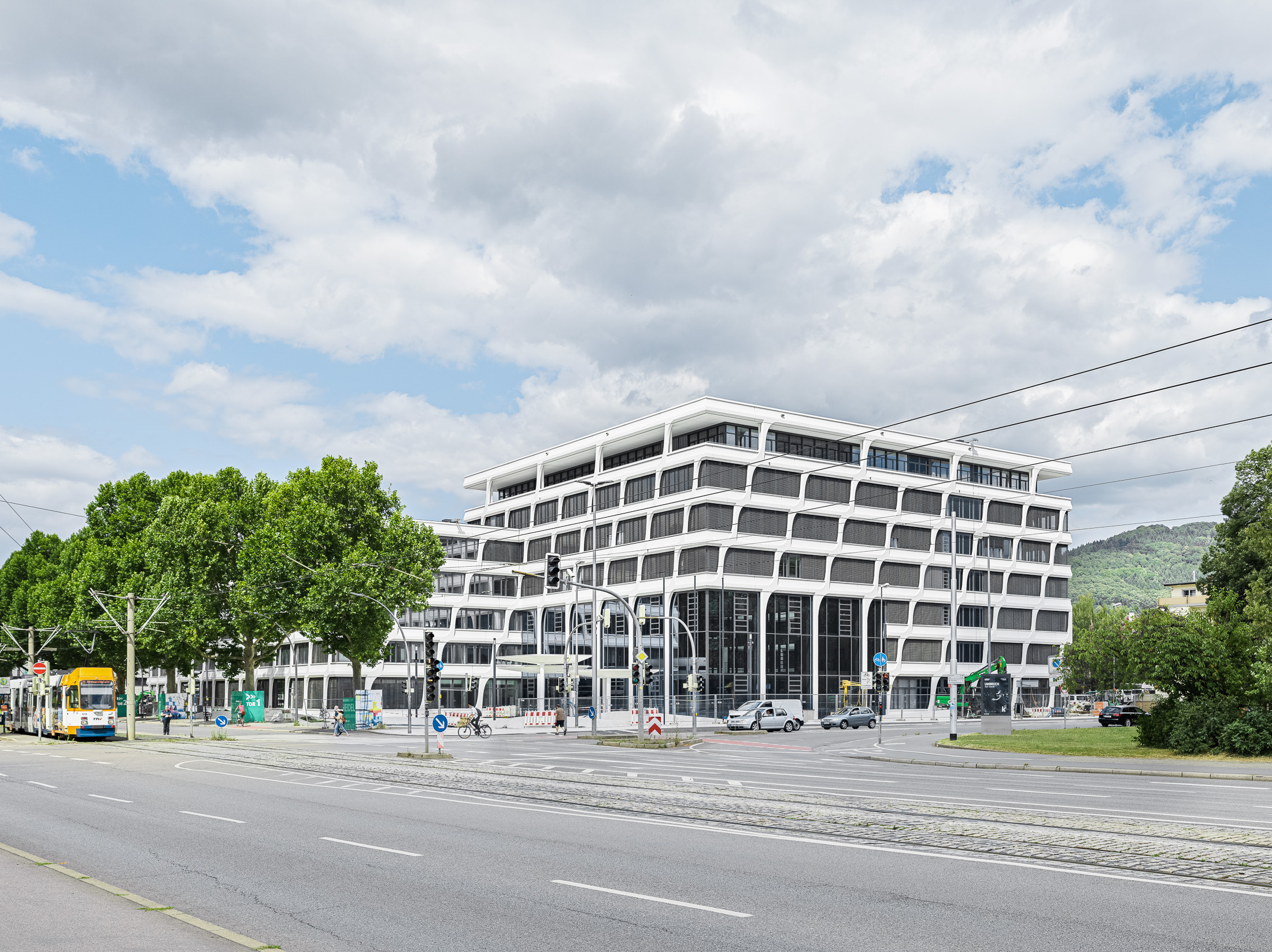 Modern office building, to the left a tram and trees, hills in the background