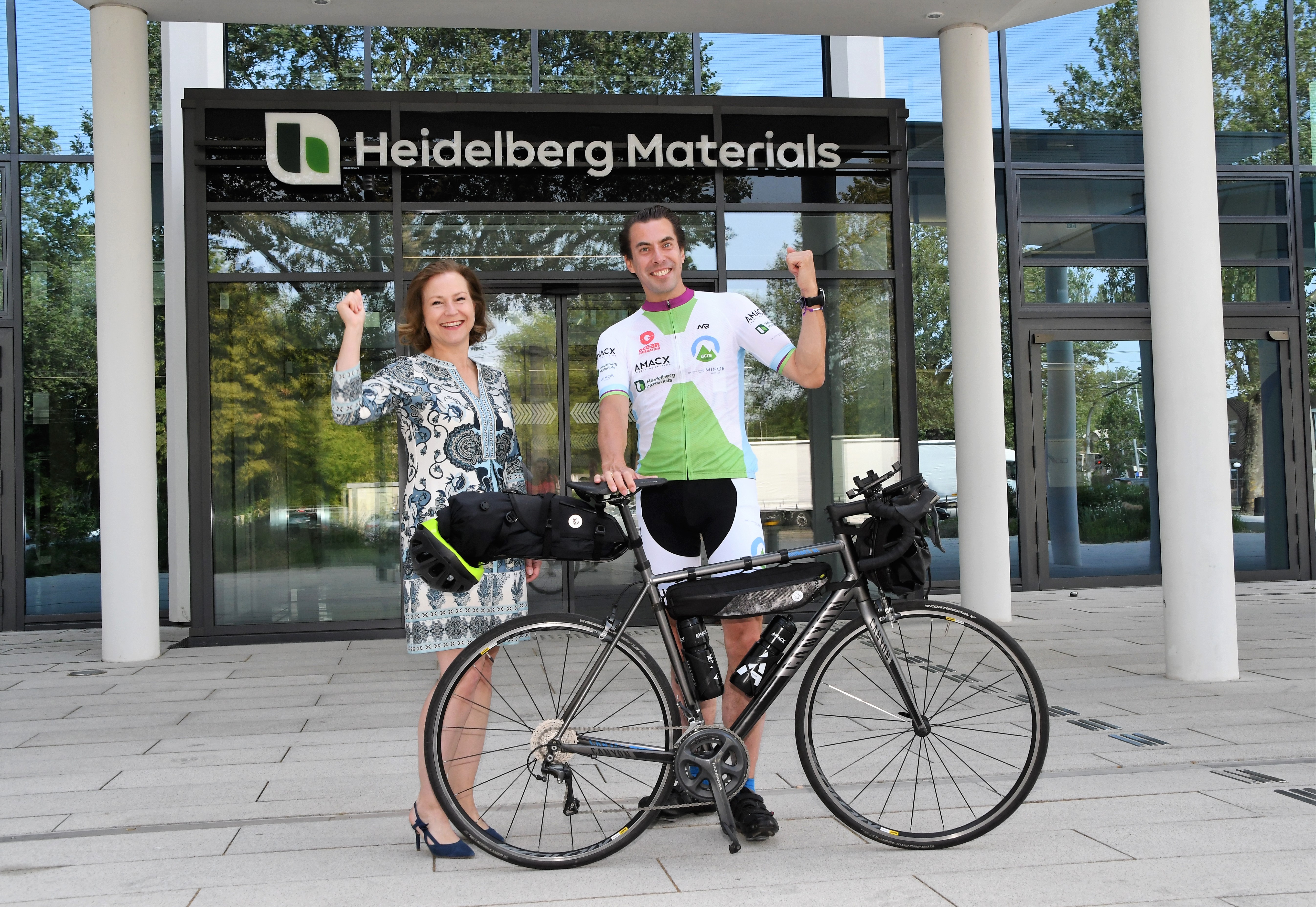 Ein Mann mit einem Fahrrad steht zusammen mit einer Frau vor der Hauptverwaltung von Heidelberg Materials