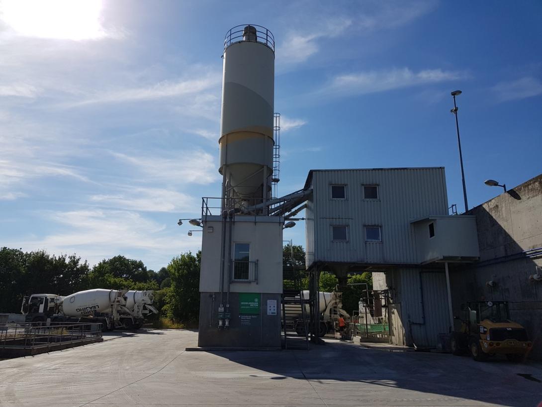 Industrial building with round silo, next to it is a ready-mixed concrete truck.