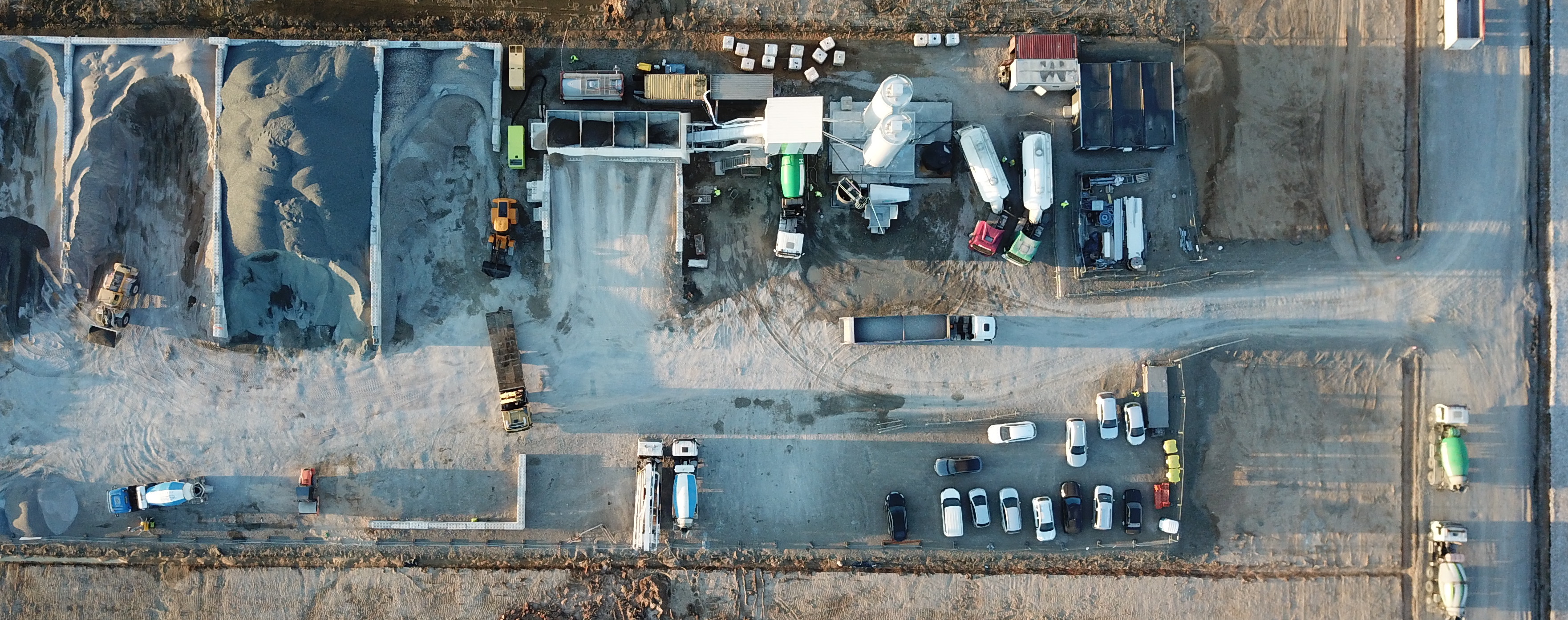 Bird's eye view of the construction site: various building machines, trucks, cars and silos