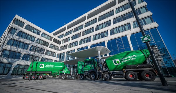 Two green ready-mix trucks are parked in front of the entrance to the Heidelberg Materials headquarters