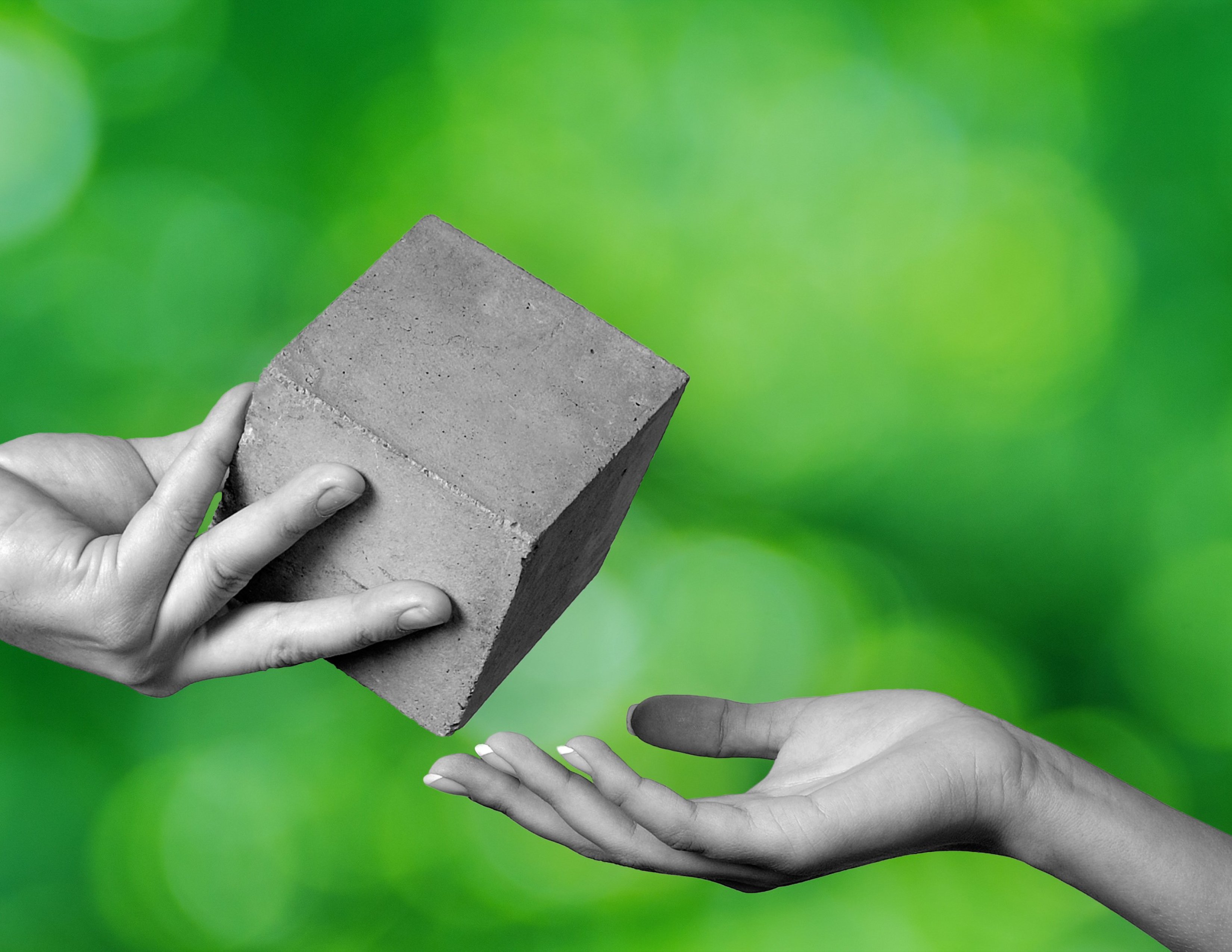 A hand is holding a cubic-formed concrete block giving it to another person