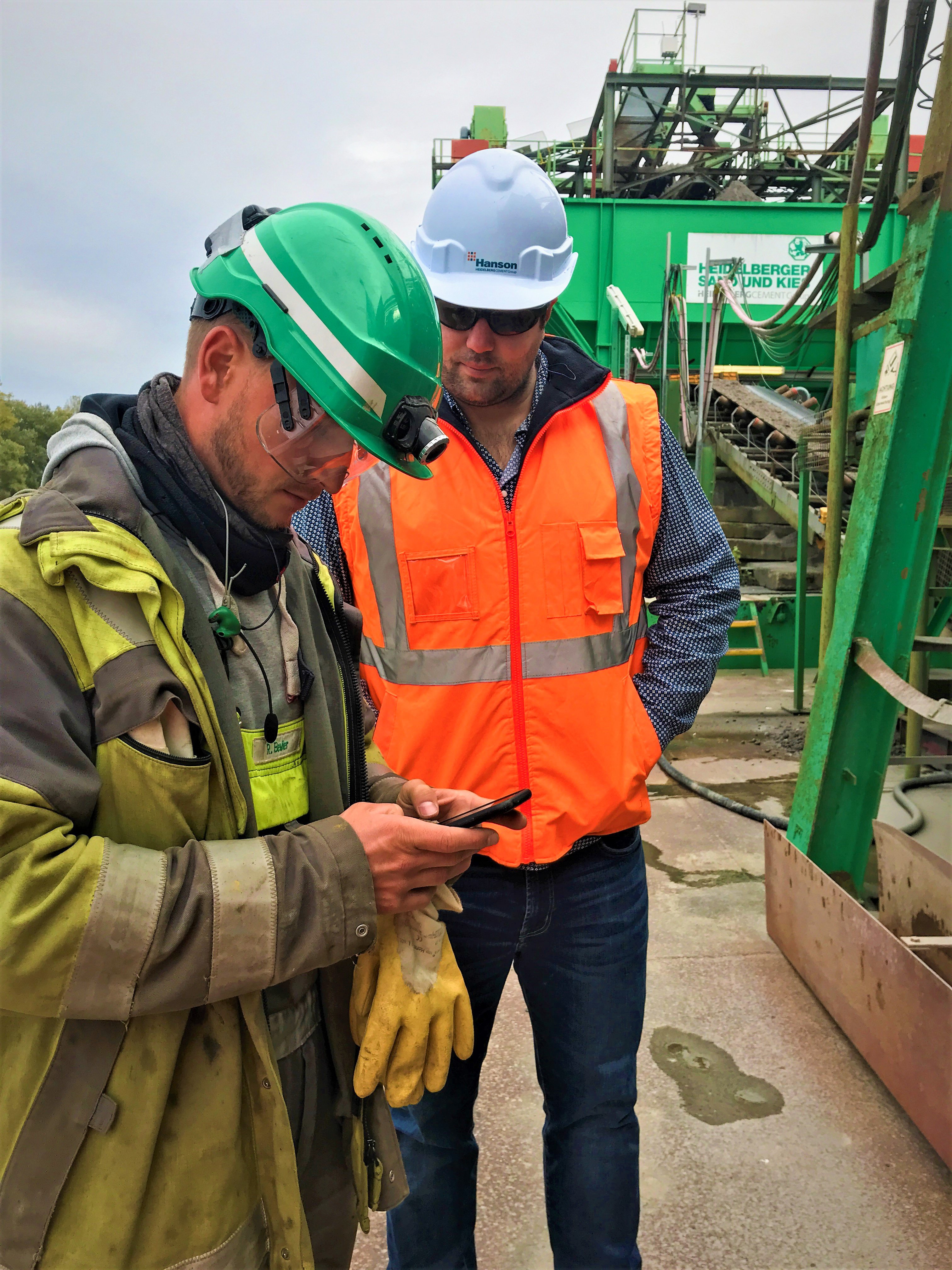 Two men in construction clothes are looking at a mobile phone