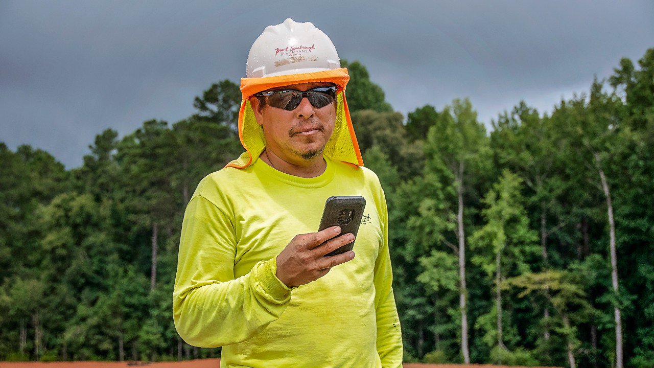 A man is holding a mobile phone, there is a forest behind him