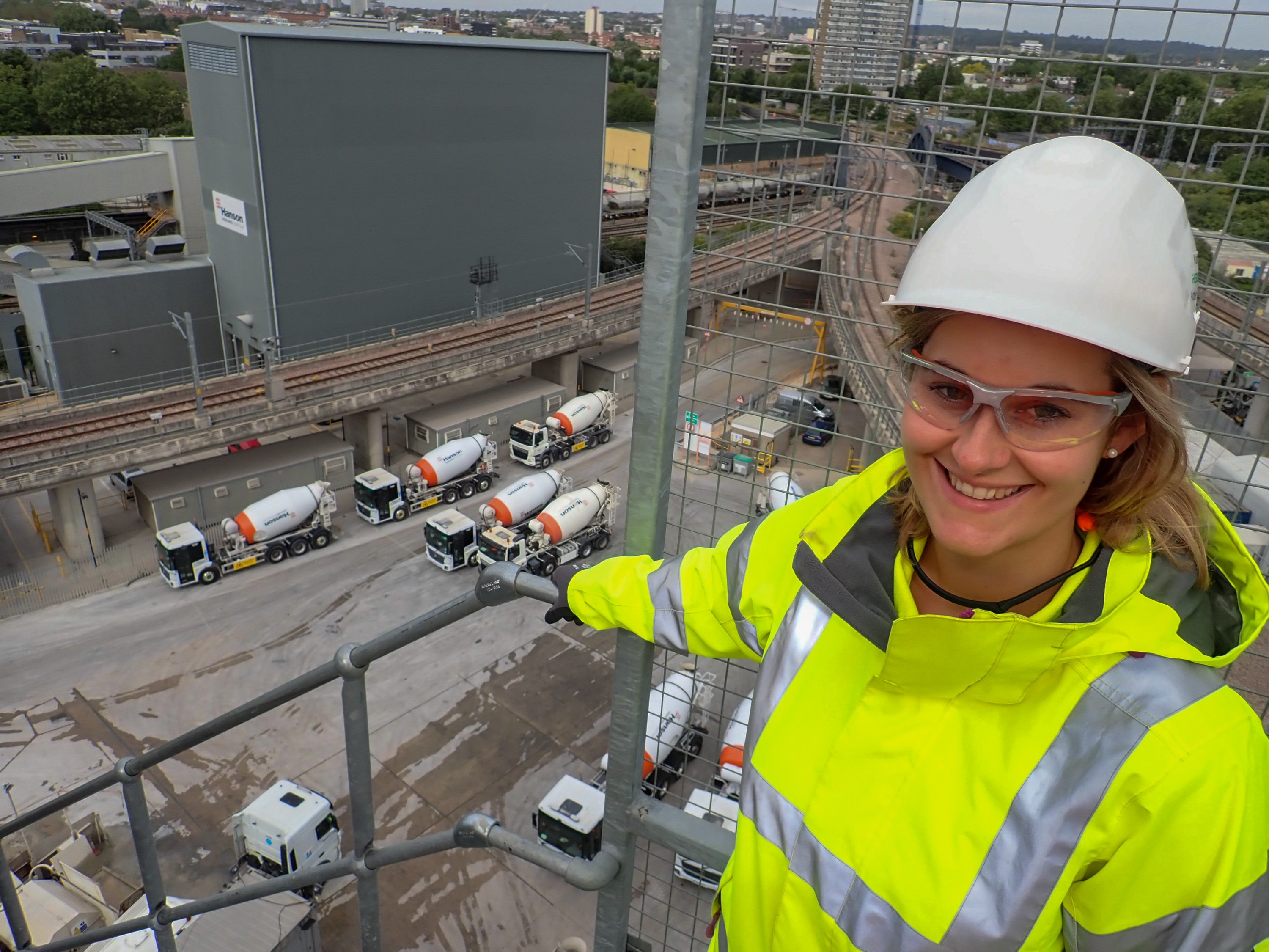 Frau mit Bauhelm steht auf einer Industrieanlage, unten stehen Betonmischfahrzeuge