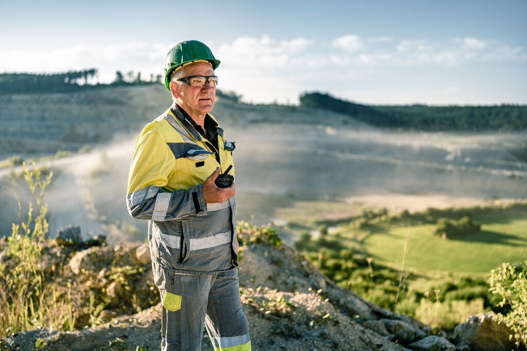 A man in construction clothes and helmet is standing before a quarry