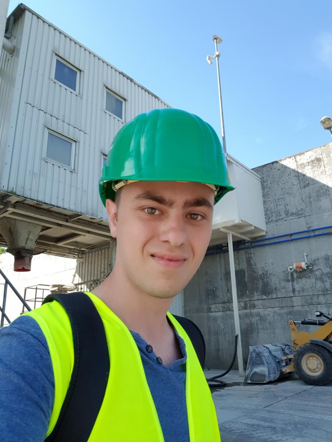 Junger Mann mit Schutzhelm, im Hintergrund ein Industriegebäude