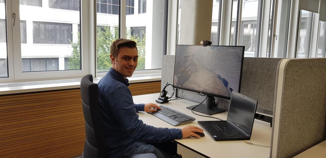 Young man at a desk with laptop, screen, keyboard and headset