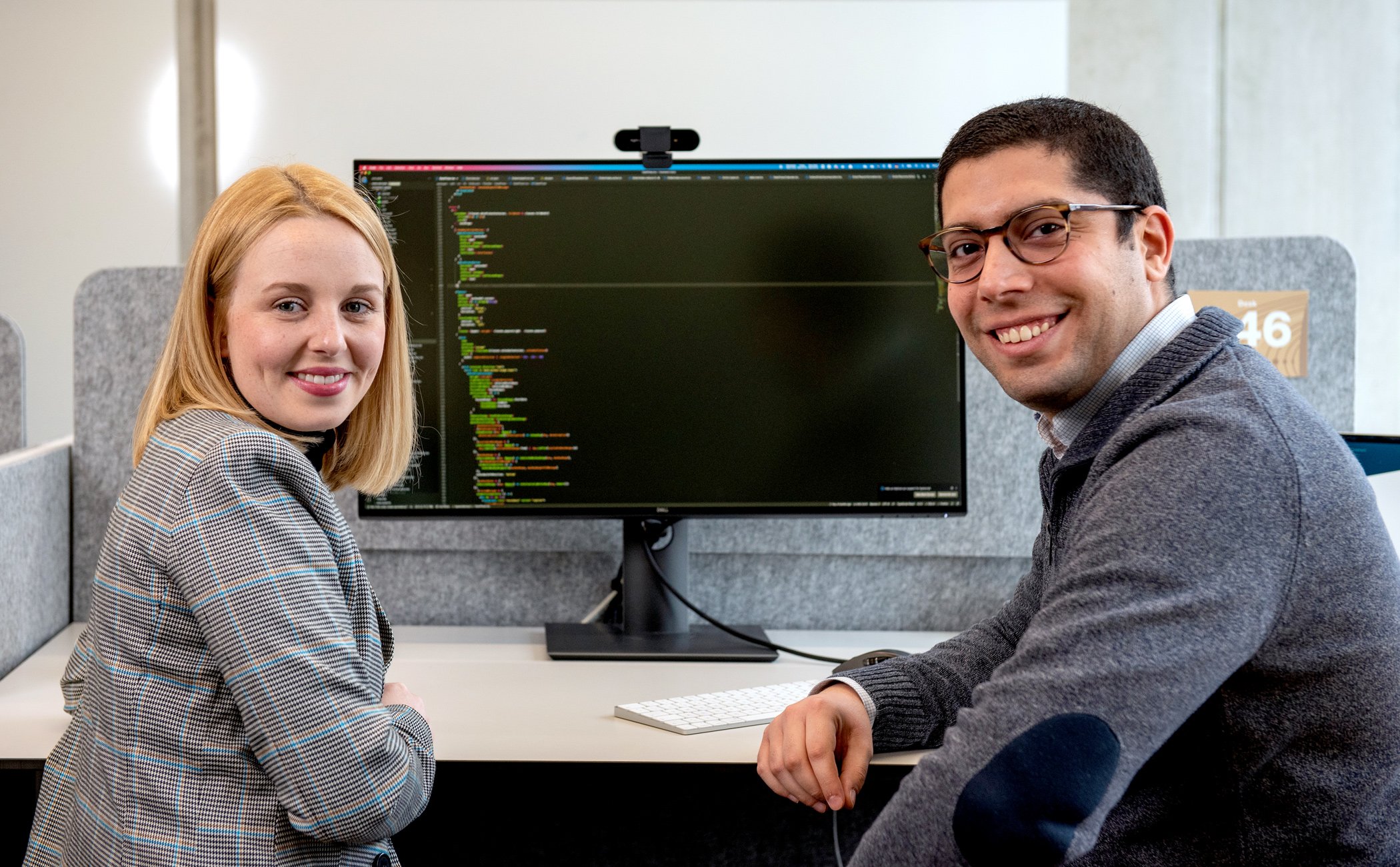 Two coworkers are sitting in front of computer with code on it