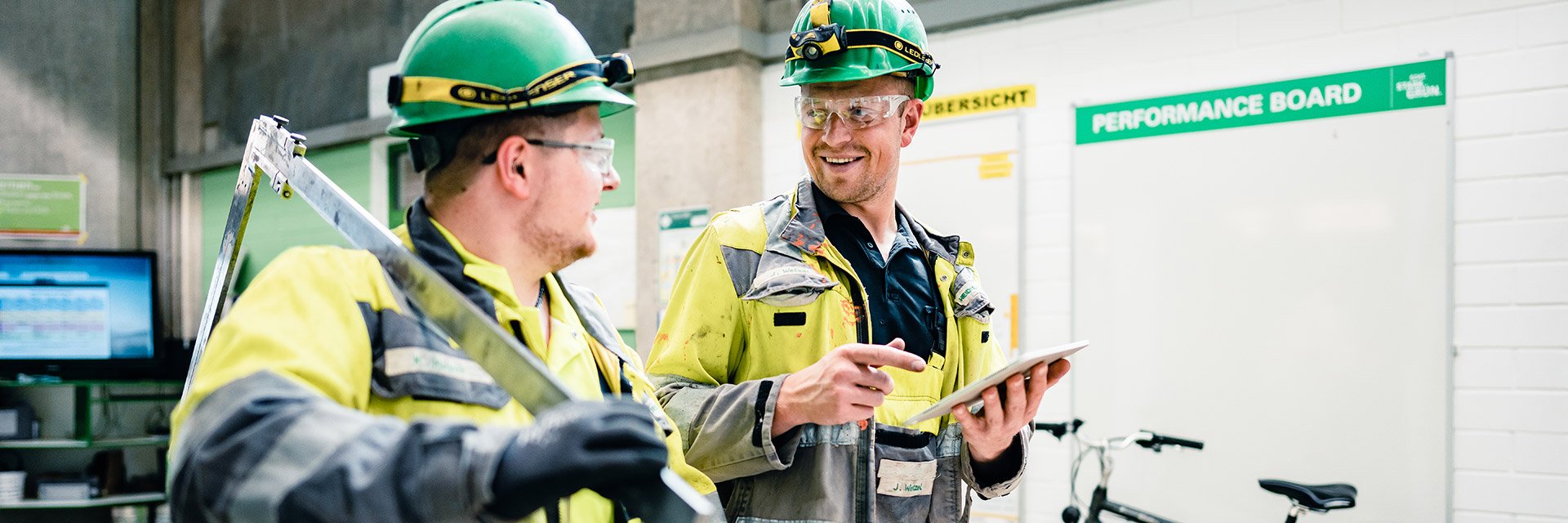 Two graduates in workwear and helmets talking to each other, both are wearing safety glasses
