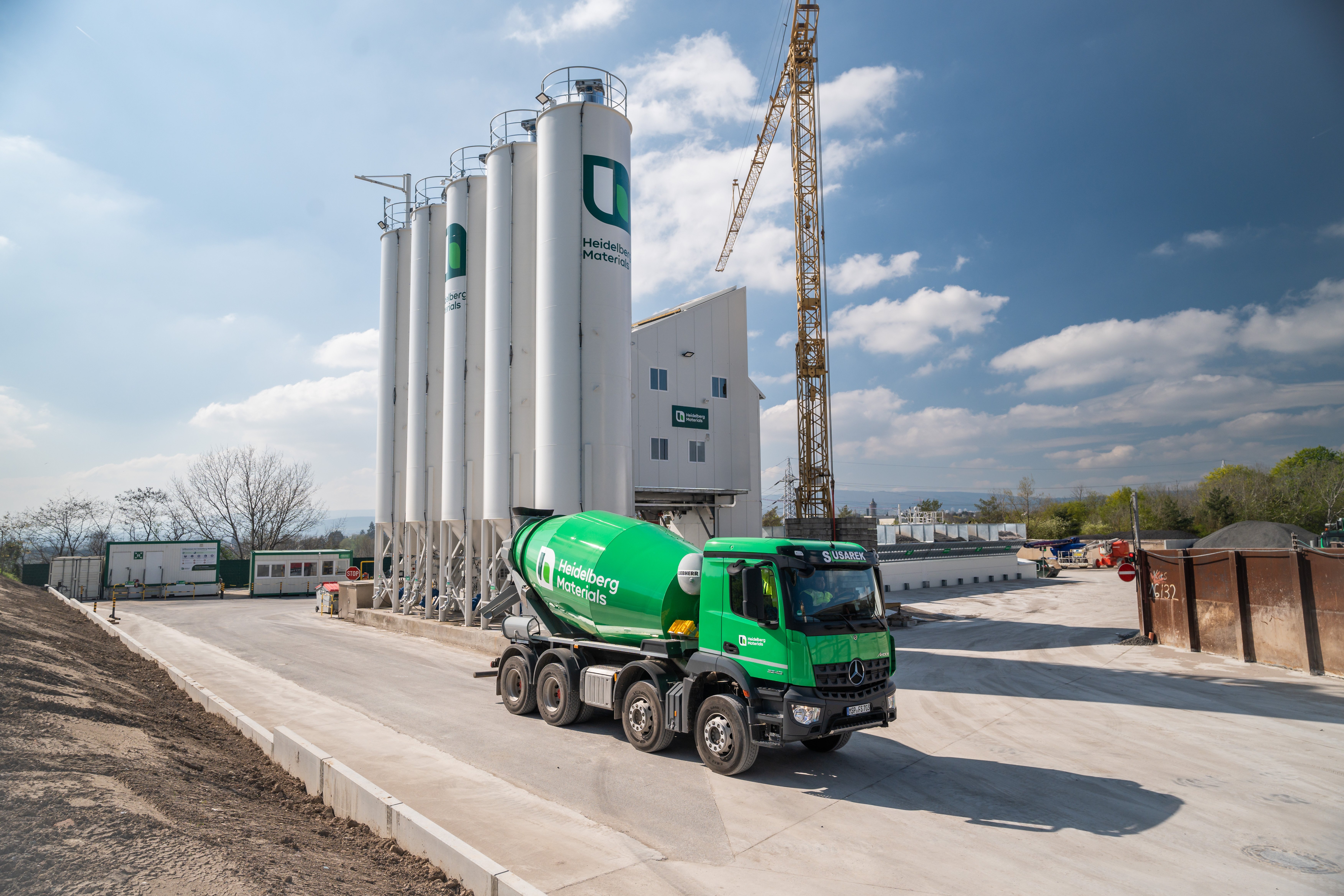 Green ready-mix truck on industrial site, silos and a crane behind it