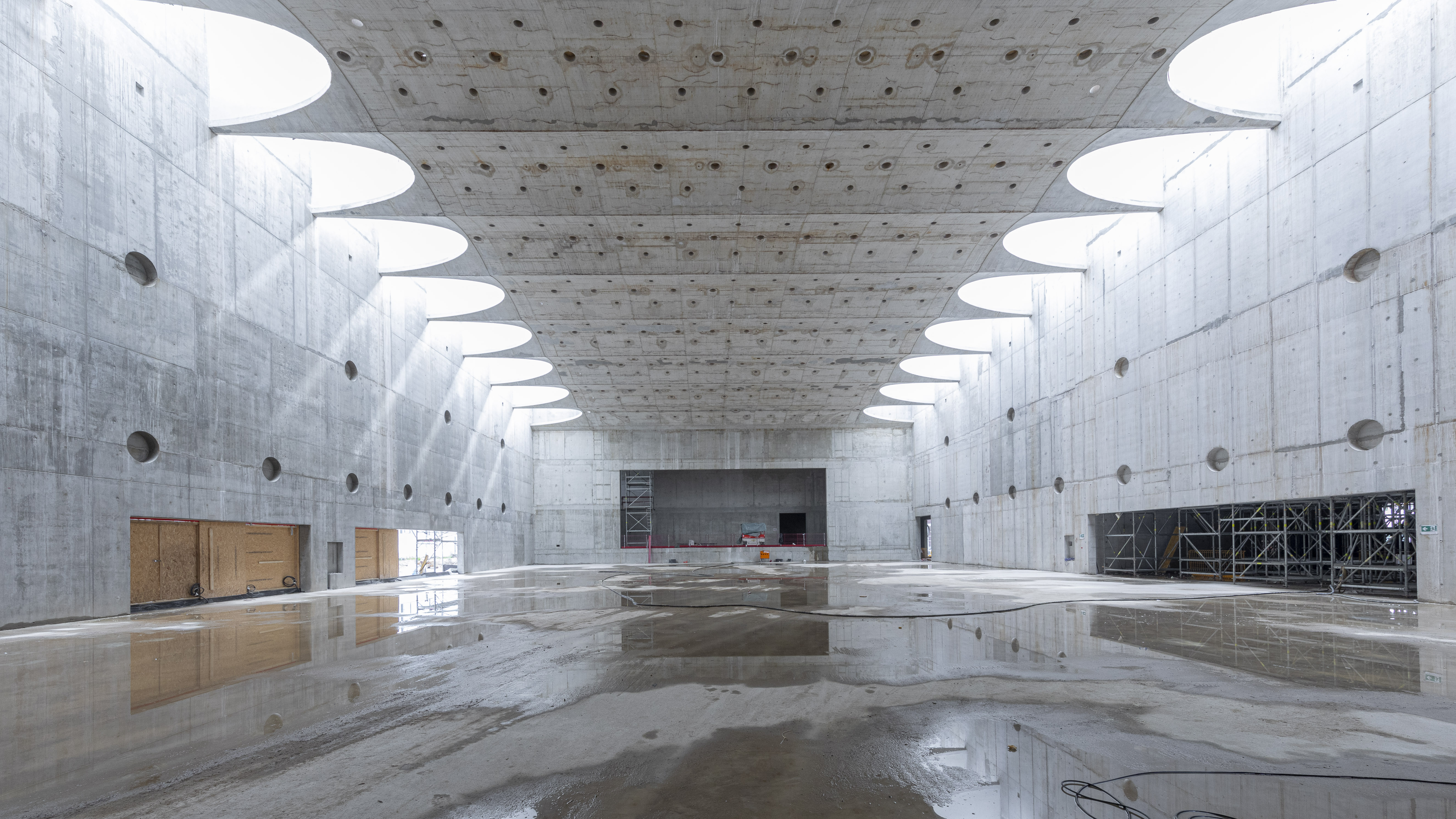 View into a large hall in shell construction, floor, ceiling and walls made of concrete, skylight comes through open semicircles at the ceiling