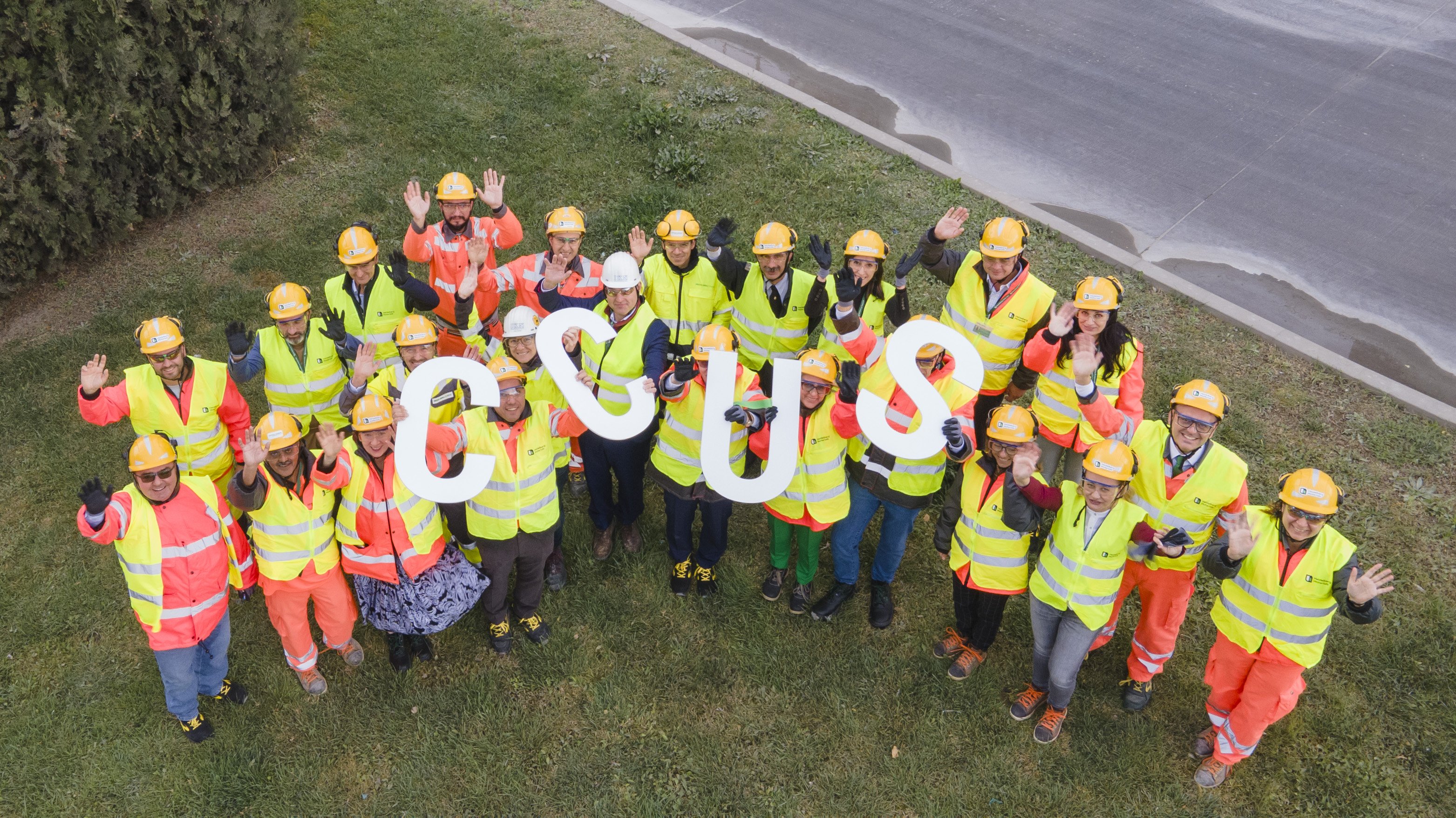 Aerial view of employees in protective clothing and with hard hats holding the letters CCUS in the air