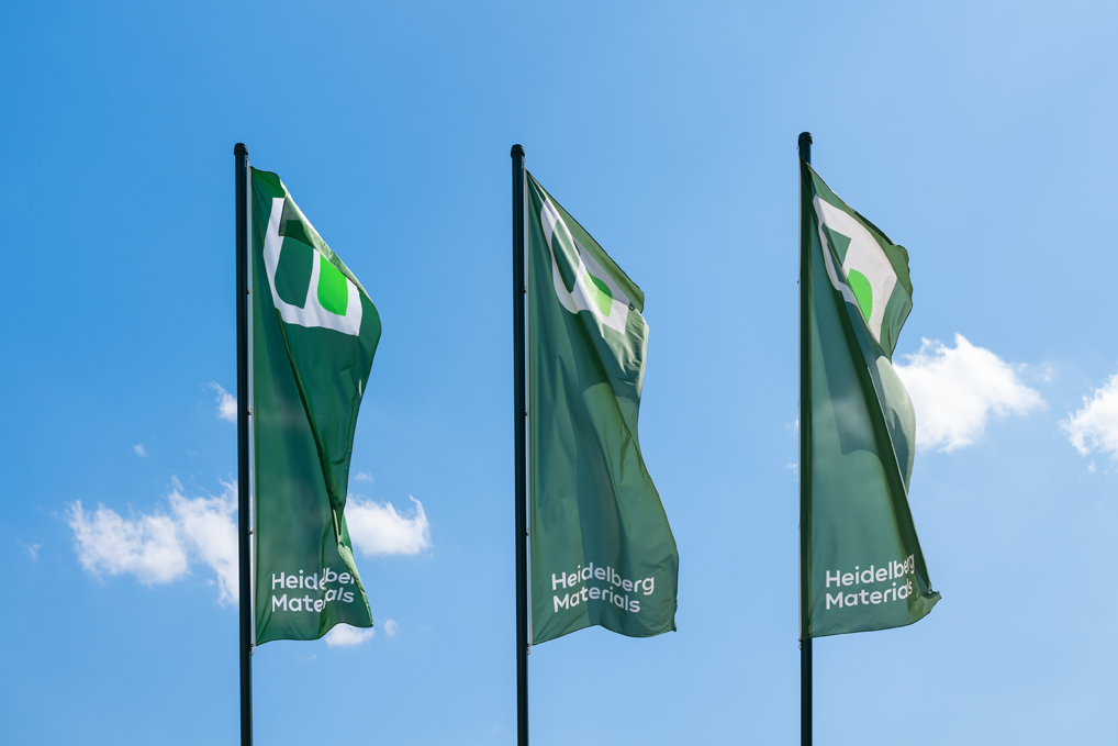Drei grüne im Wind wehende Fahnen mit dem Heidelberg-Materials-Logo