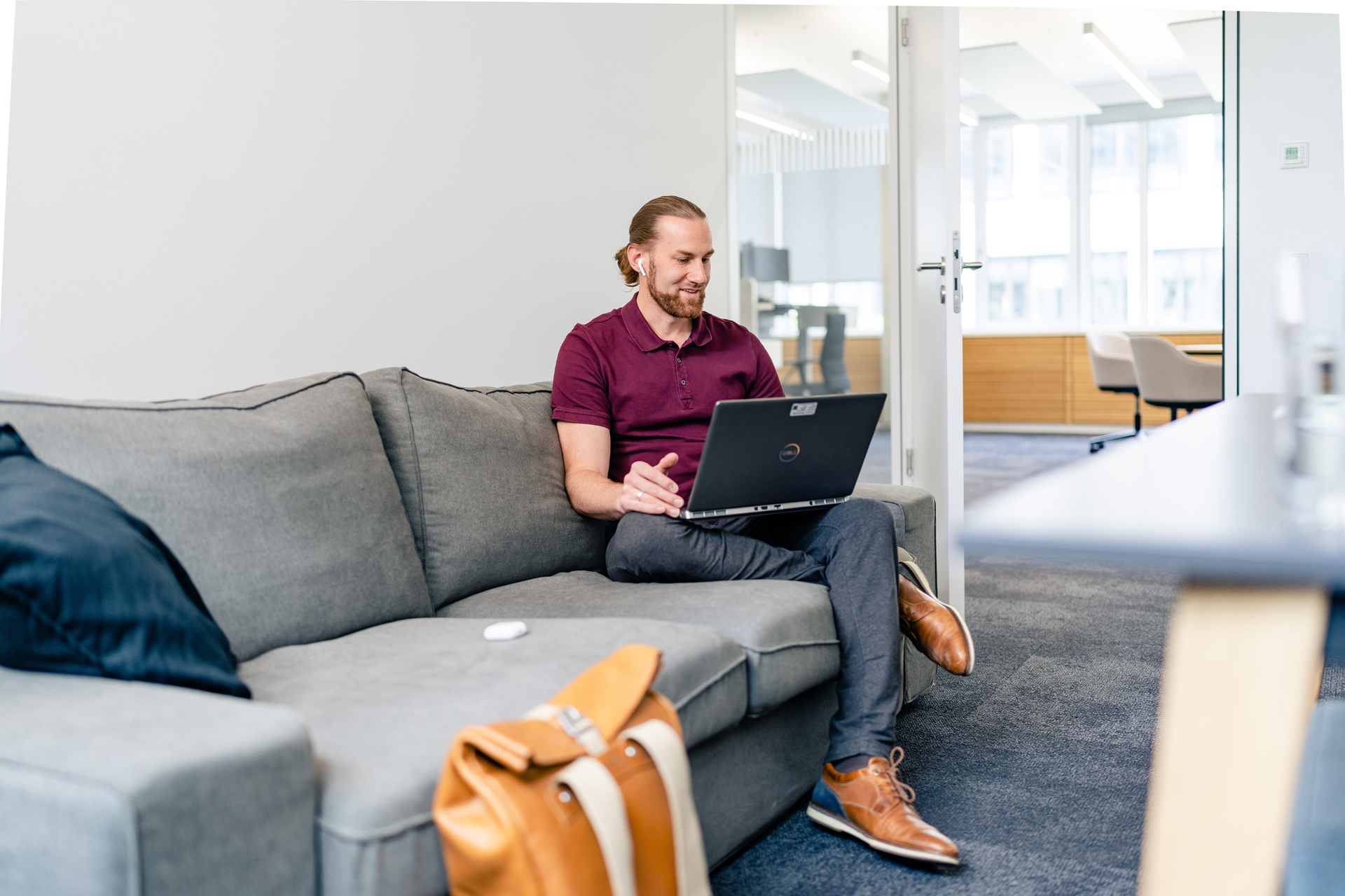 Young male guy sitting on a grey couch with a notebook on his lap