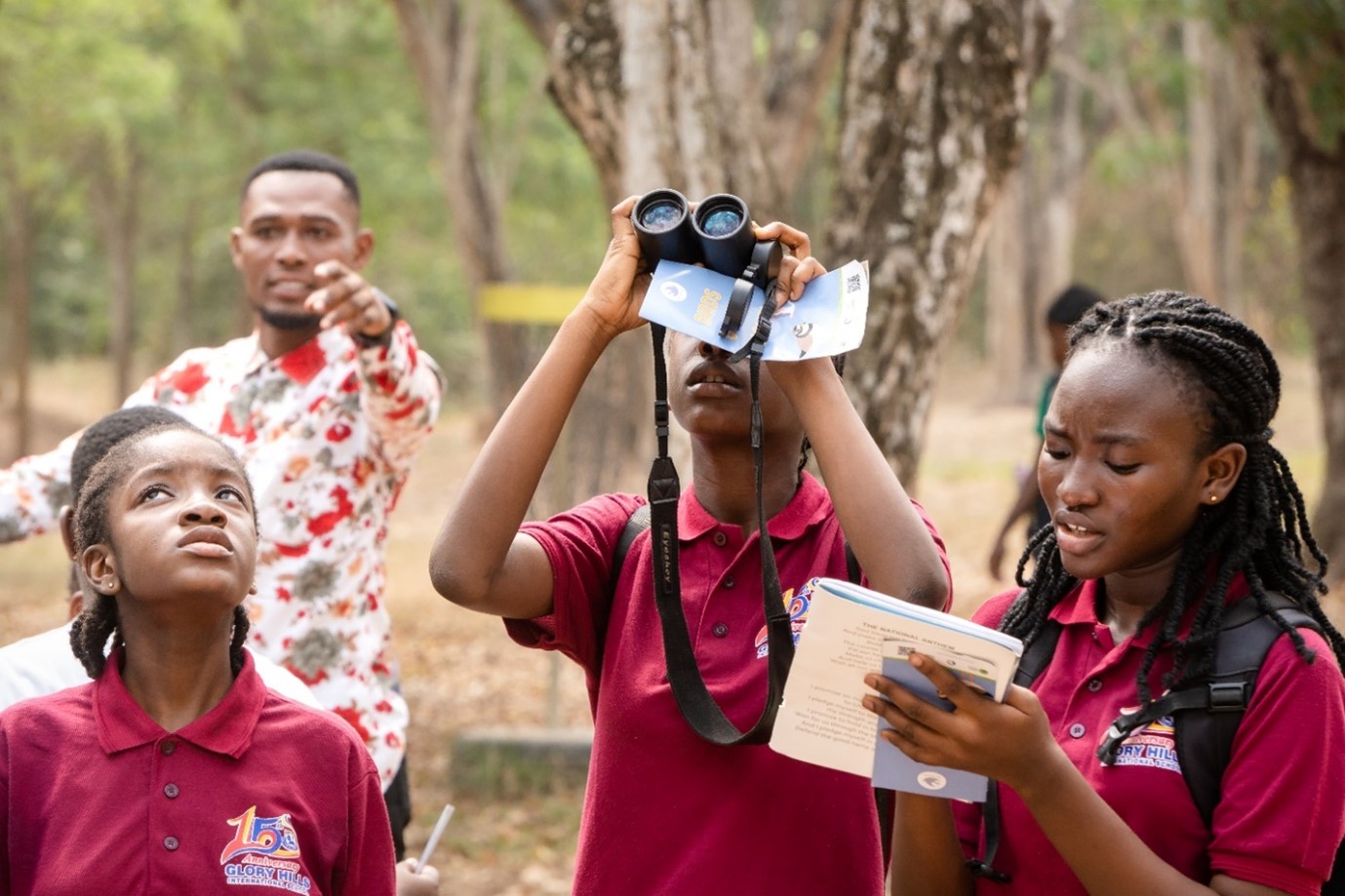 Pupils watch birds, one holds binoculars, one notes something down