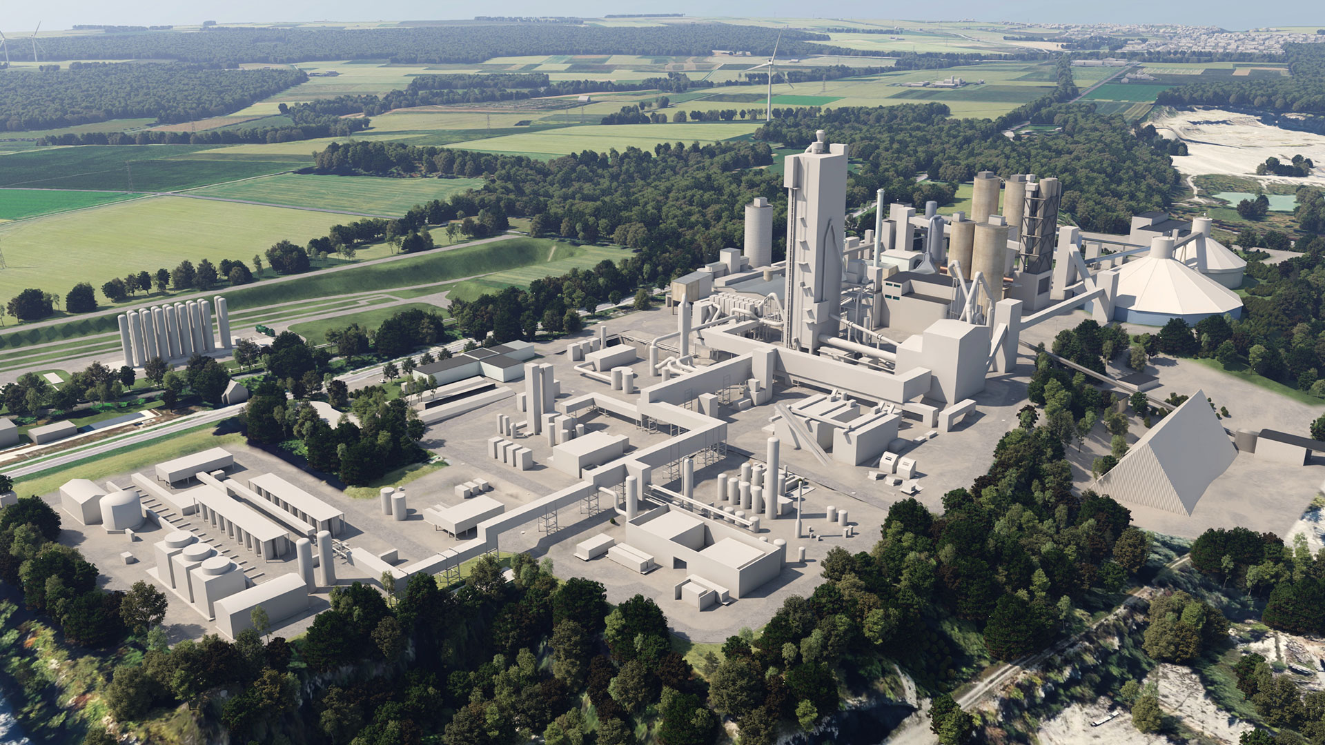Aerial view of a large industrial cement plant surrounded by green fields and dense trees. The facility includes multiple tall silos, chimneys, warehouses, and roads connecting the structures. 