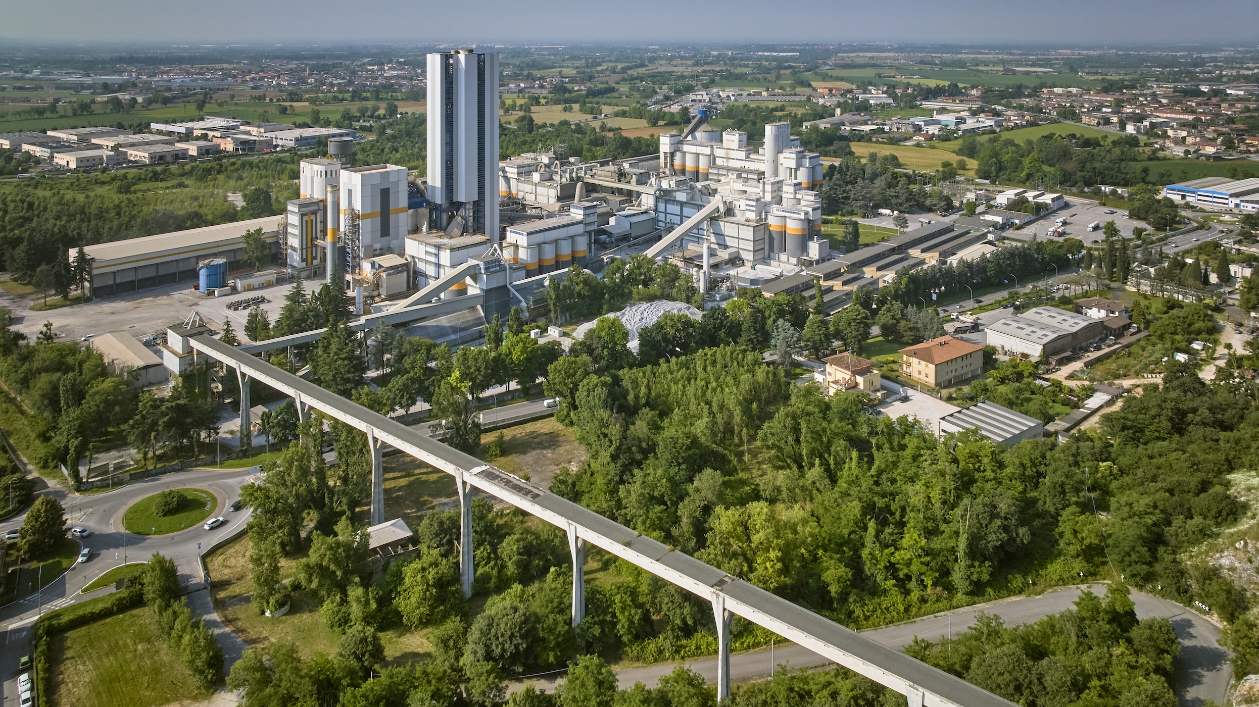 A cement plant surrounded by greenery and nearby infrastructure.