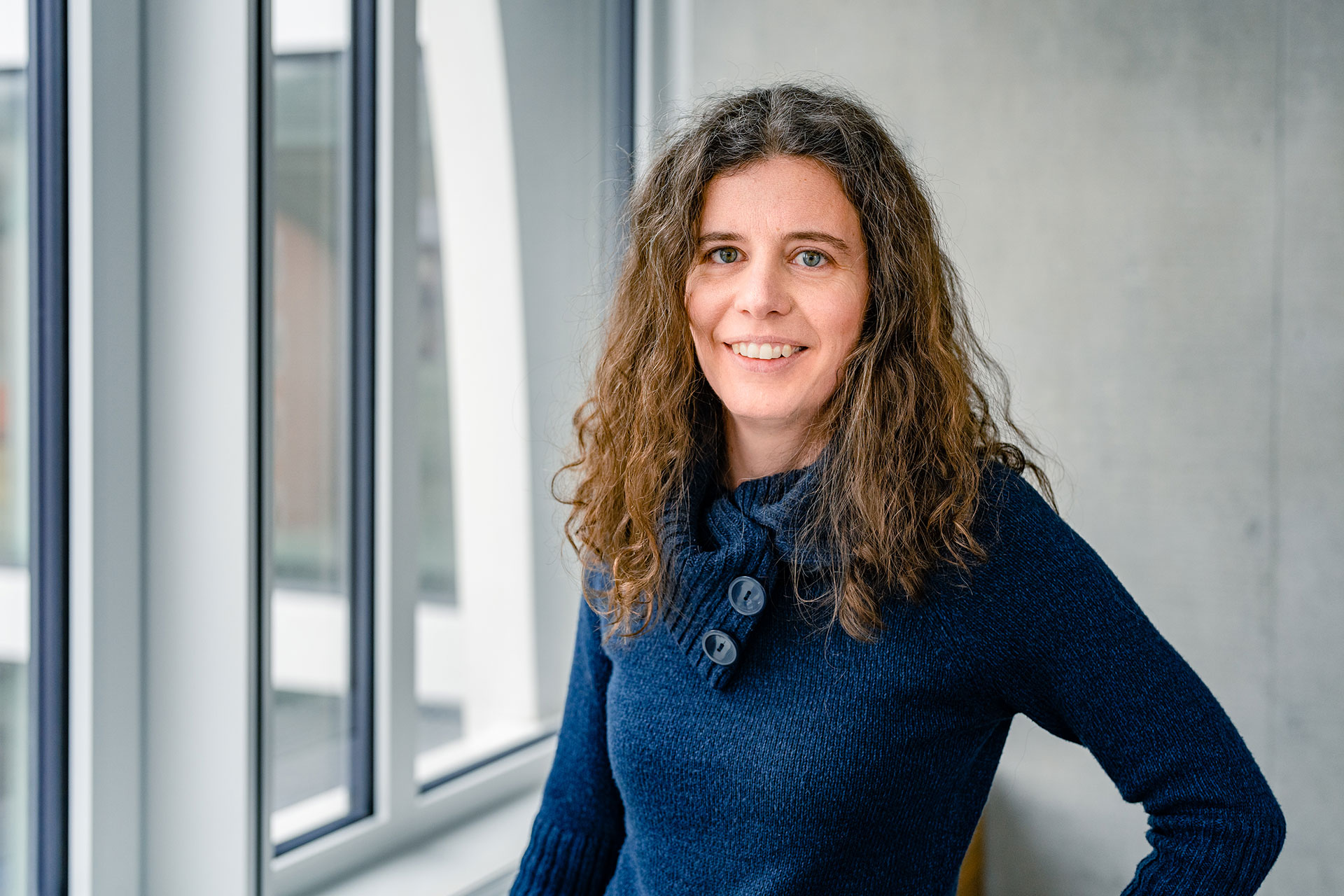 Eszter Harsányi in a dark blue jumper in front of a window and a grey concrete wall