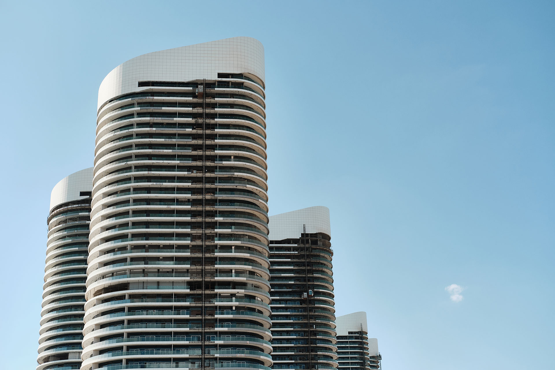 Drei moderne Hochhäuser mit geschwungenen Kanten und einem eleganten Design unter einem strahlend blauen Himmel.