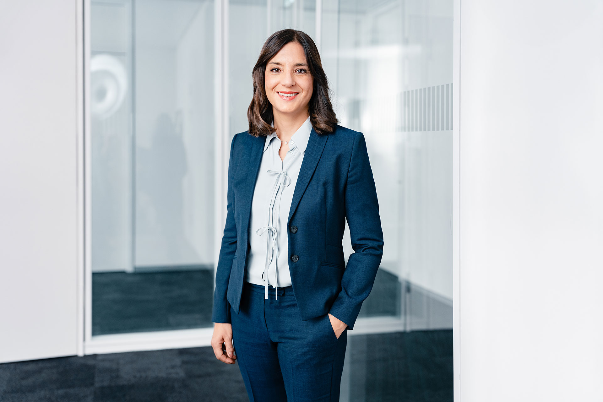 Katja Karcher in einem blauen Business-Anzug und einer weißen Bluse steht in einem modernen, hellen Büro.