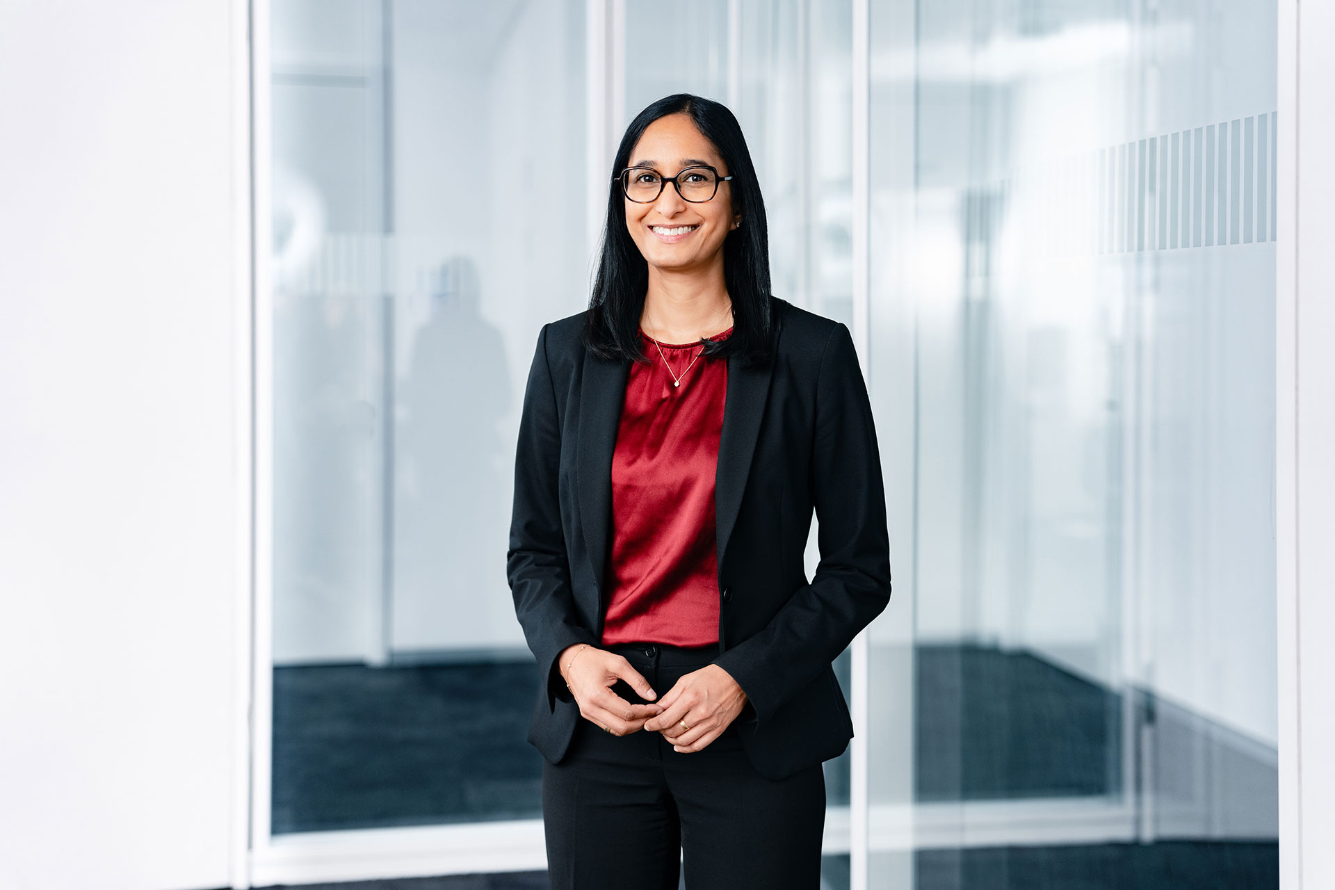 Sopna Sury in einem Business-Anzug mit roter Bluse in einem modernen Büro mit Glaswänden.
