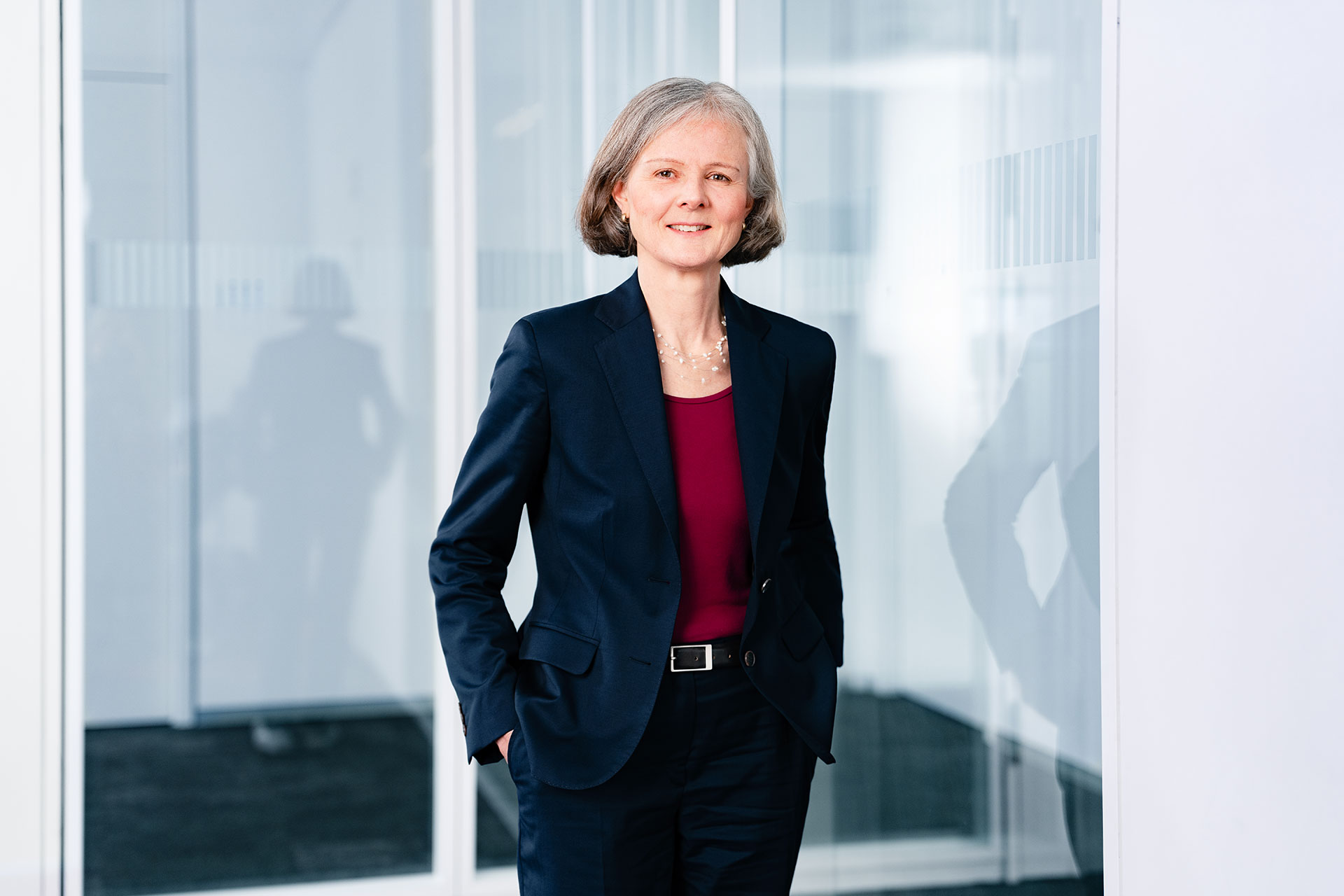 Barbara Breuninger in Businesskleidung steht in einem modernen Bürogebäude mit verglasten Wänden.