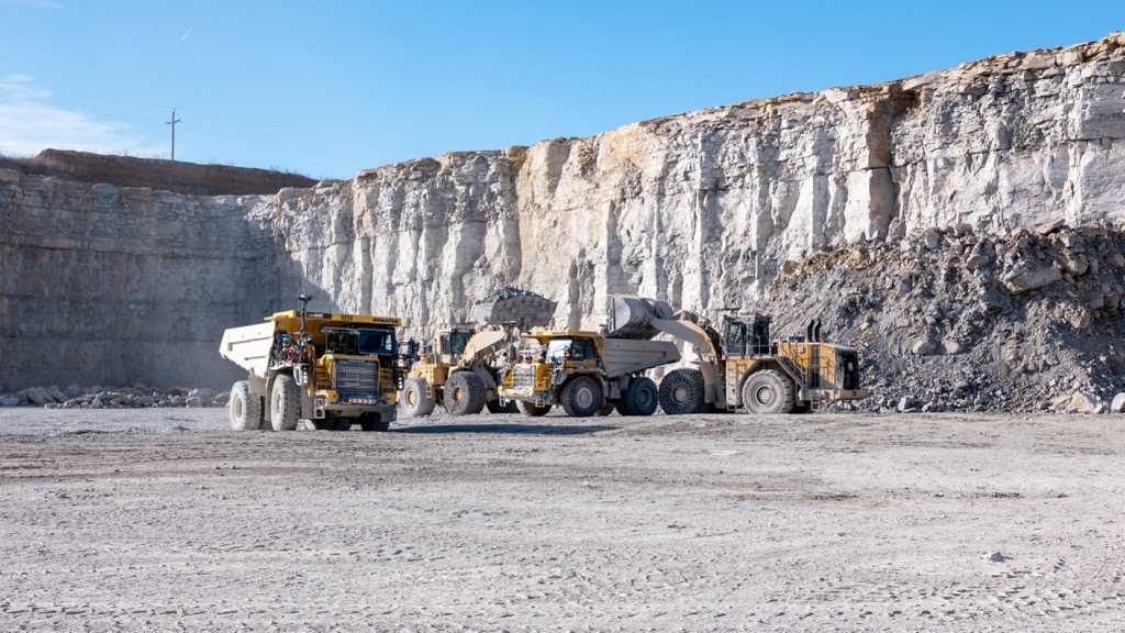 Heavy machinery operates in a large quarry with high rock walls under a clear sky.