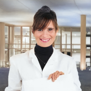 A person in a white jacket holding a document, standing in an industrial building interior.