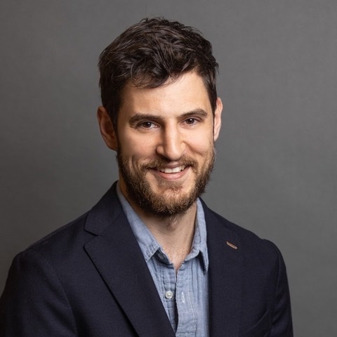 A person wearing a blazer and shirt is posed against a plain background.