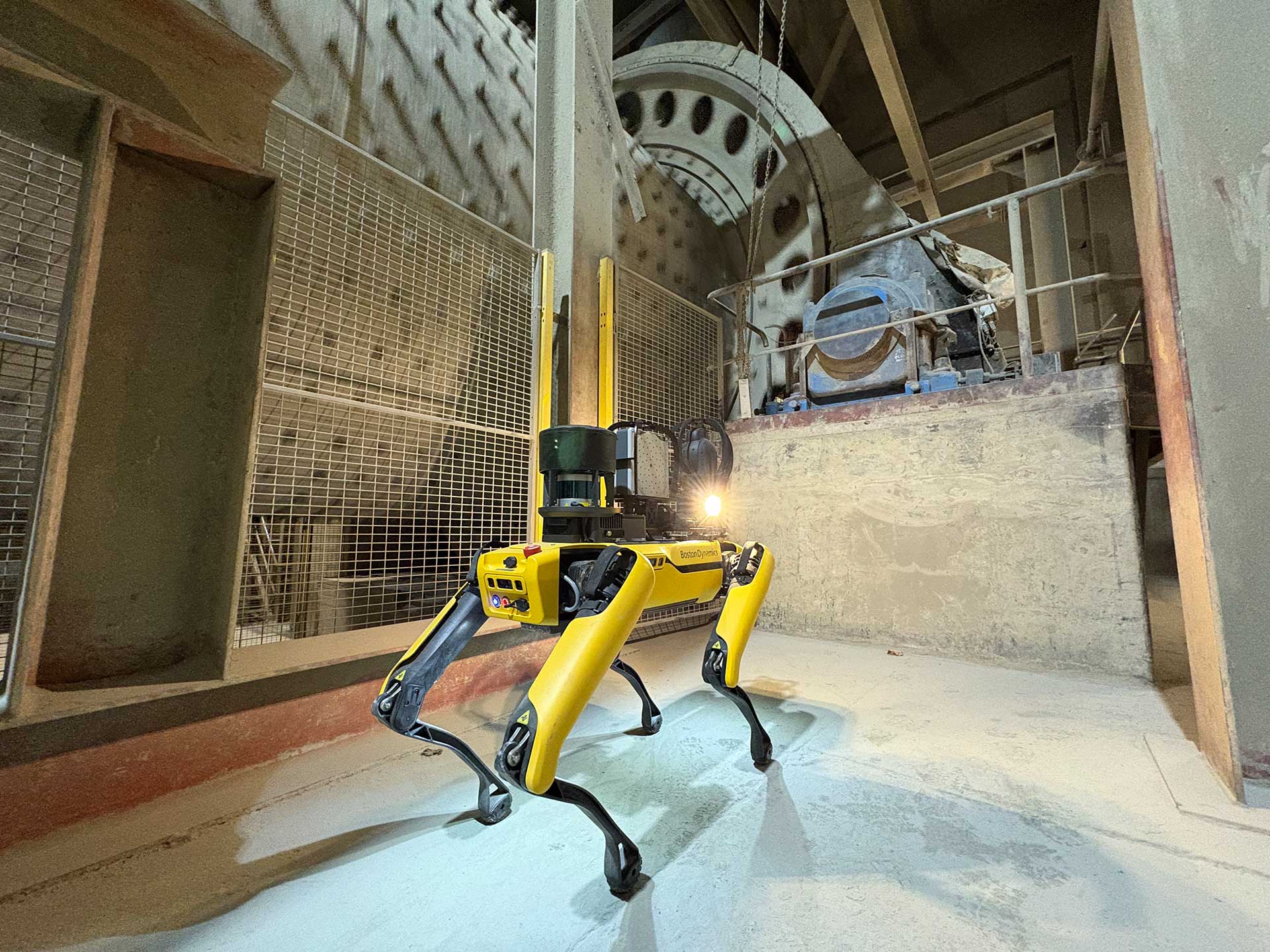 A yellow robotic dog stands in a cement plant with machinery in the background.