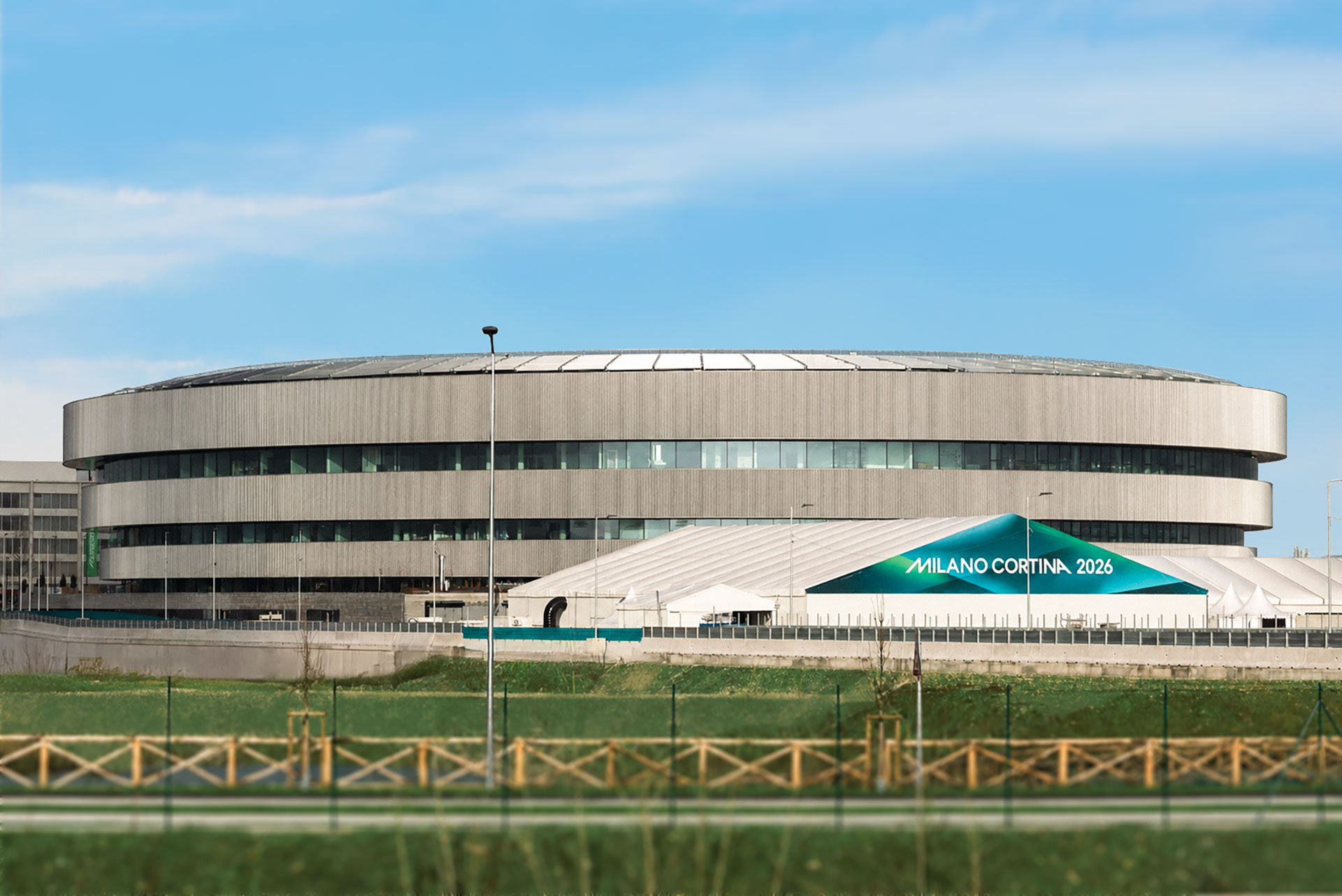 The Arena Santa Giulia, a modern circular building, surrounded by grass and fencing.