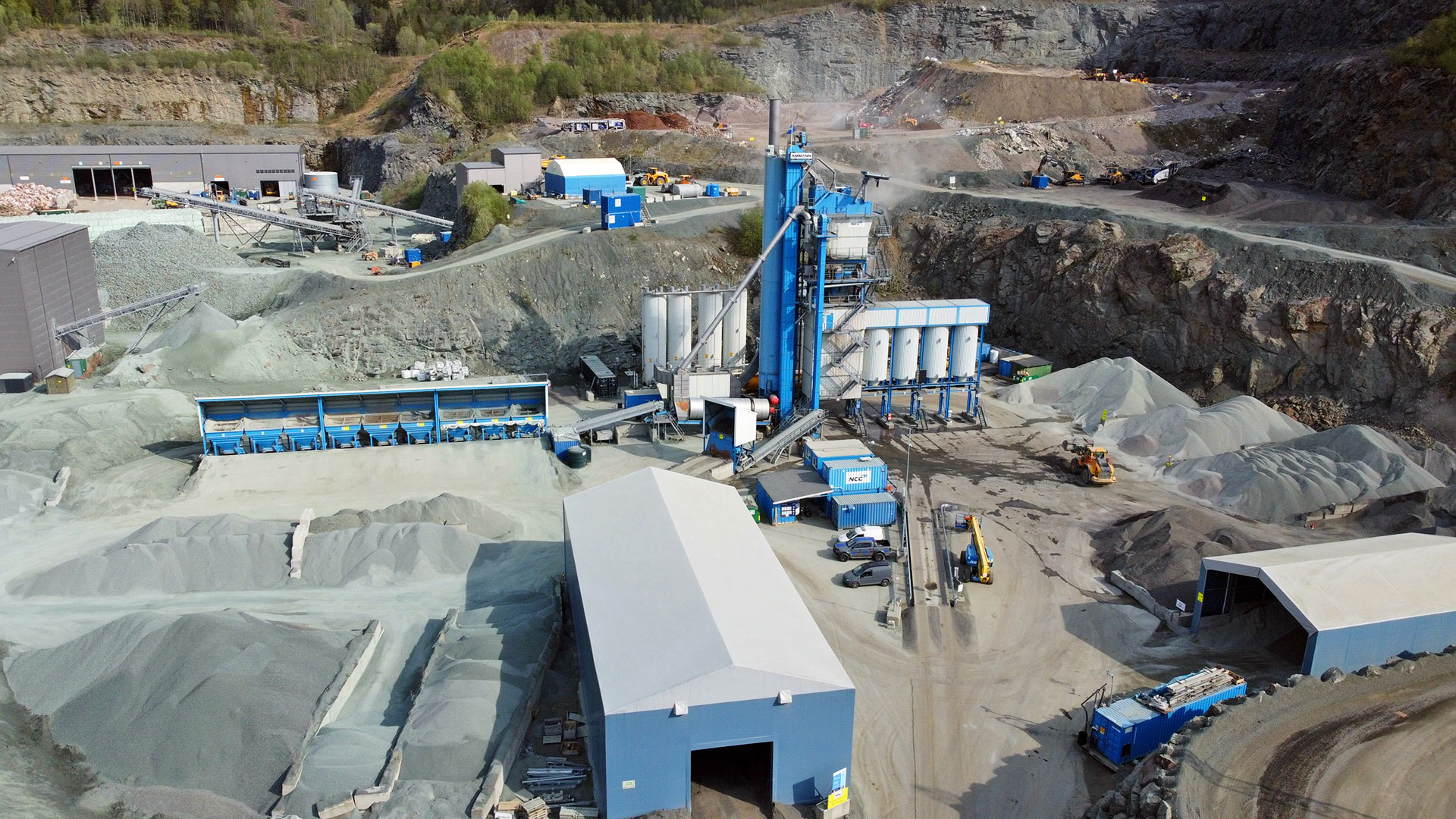 An asphalt plant with large machinery, storage facilities, and piles of raw materials used for construction.