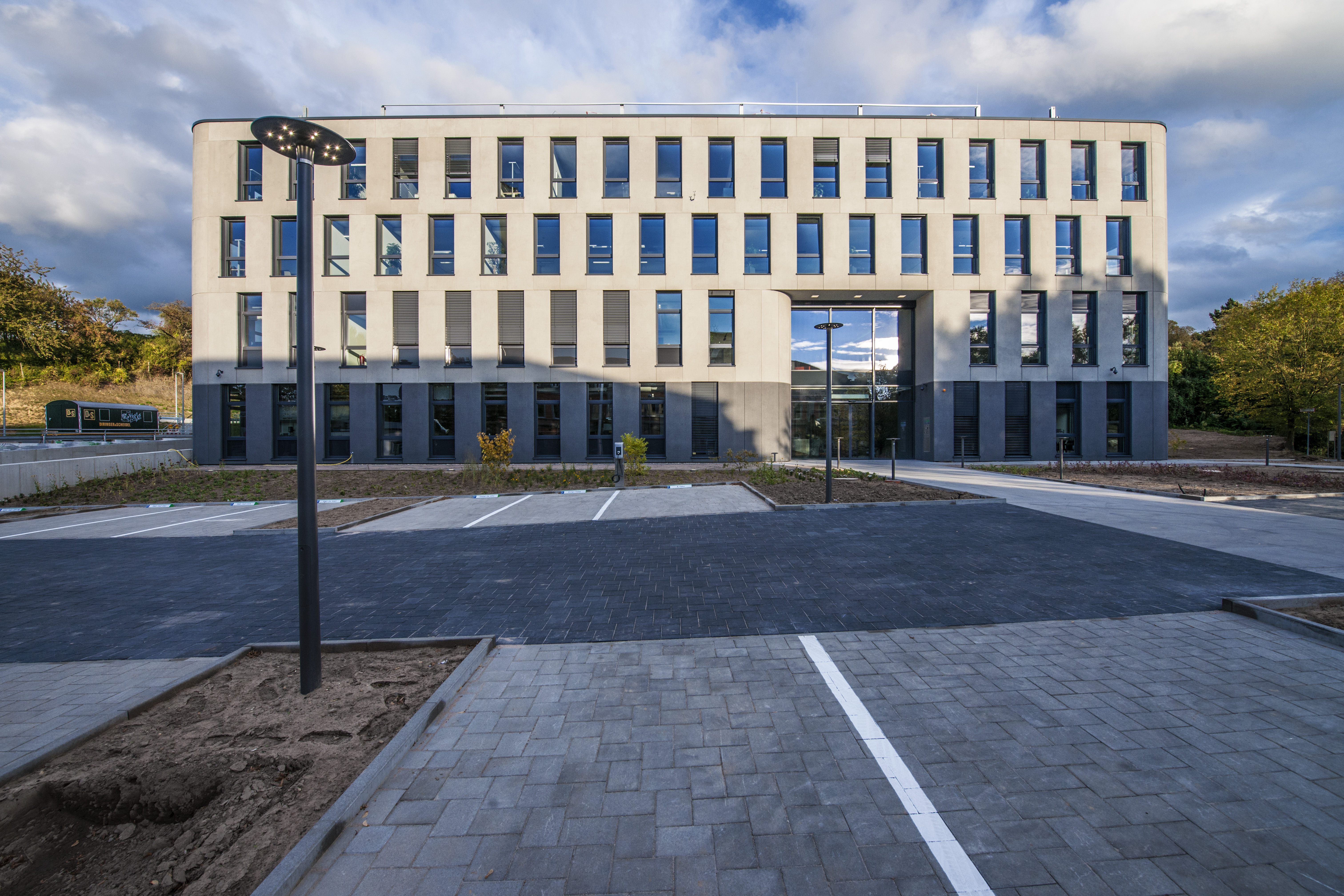 Beige office building with narrow high windows, in front of it are parking spaces