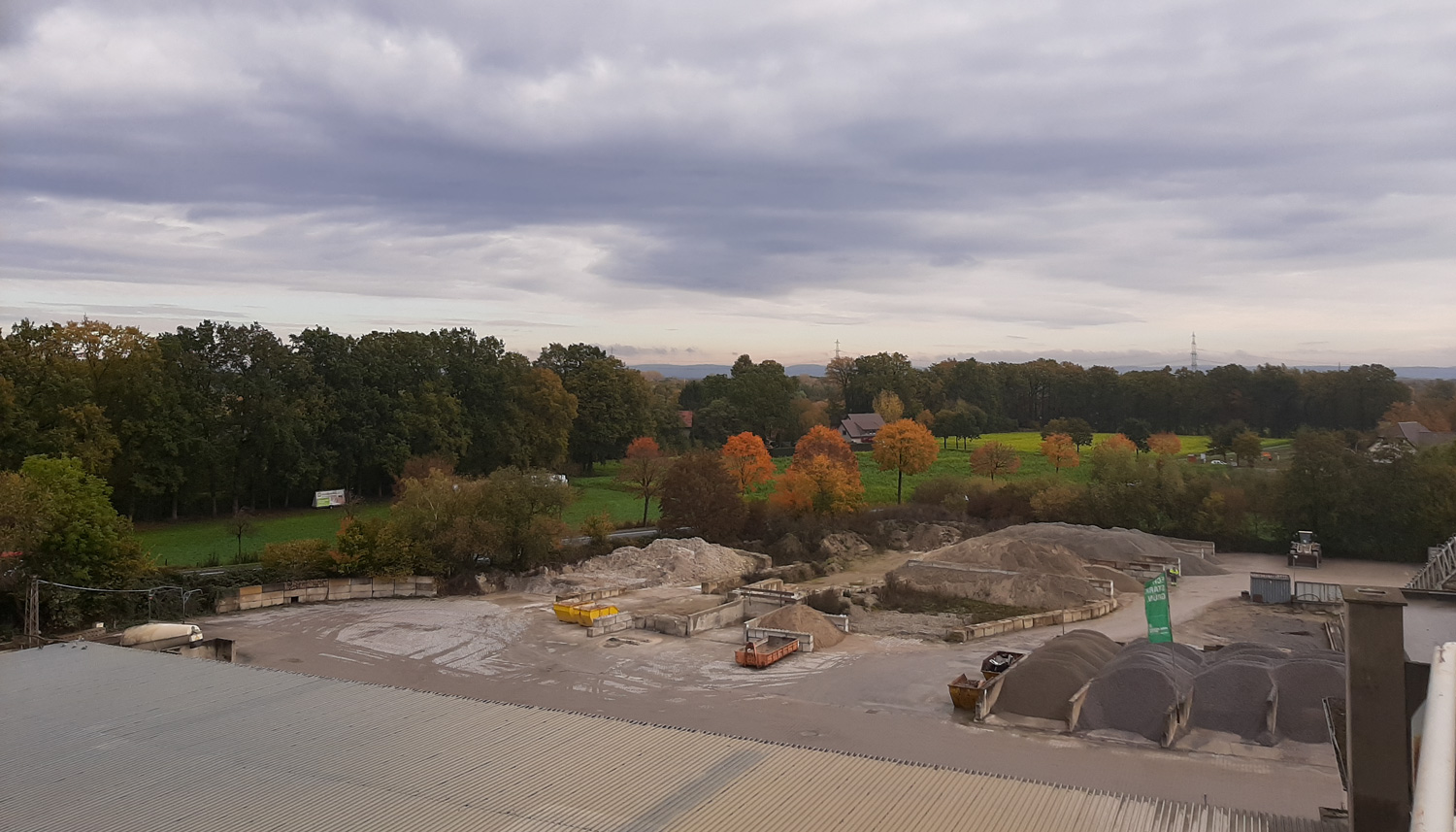 Blick auf Berge aus Sand und Splitt, dahinter grüne Landschaft mit Bäumen