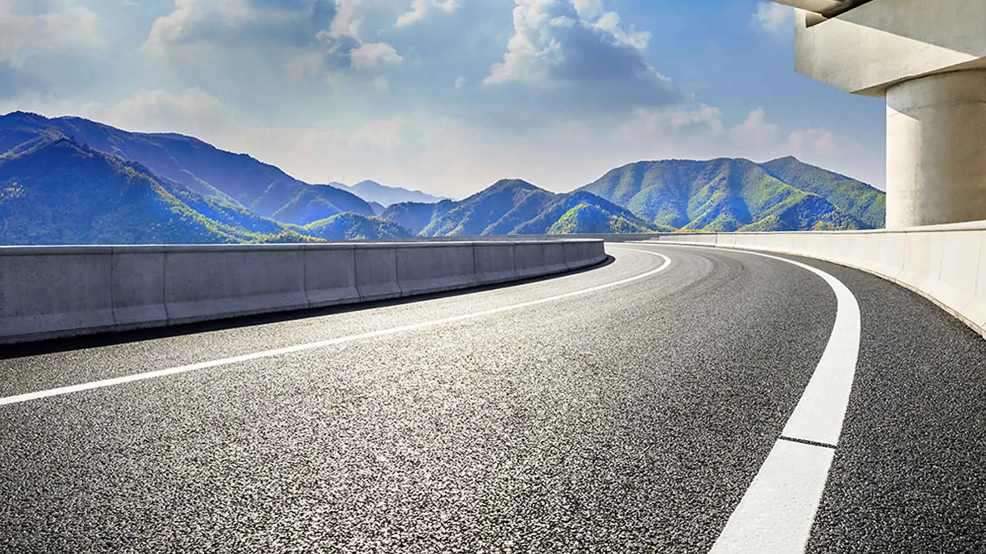 An empty road leading towards the mountains and crossed by a bridge