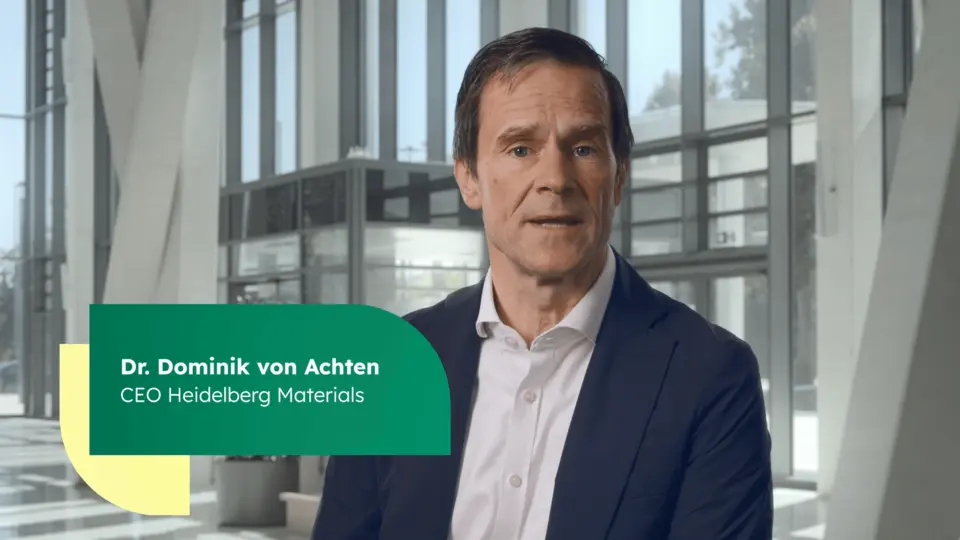 Dr Dominik von Achten in business attire is seated in a modern office environment with large windows and structural elements visible in the background.