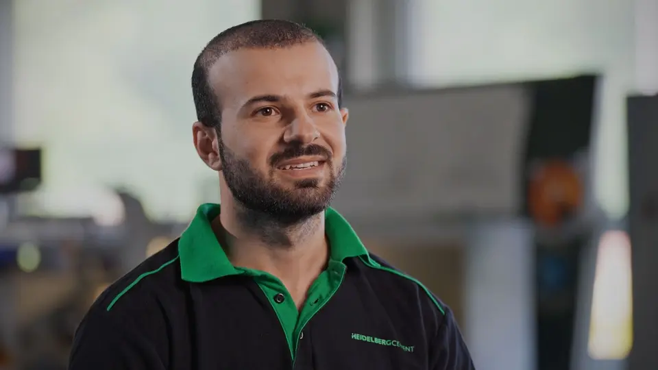 Mann mit dunklen Haaren und einem dunklen kurzen Vollbart in schwarz-grünem Poloshirt vor einem verschwommenen Hintergrund