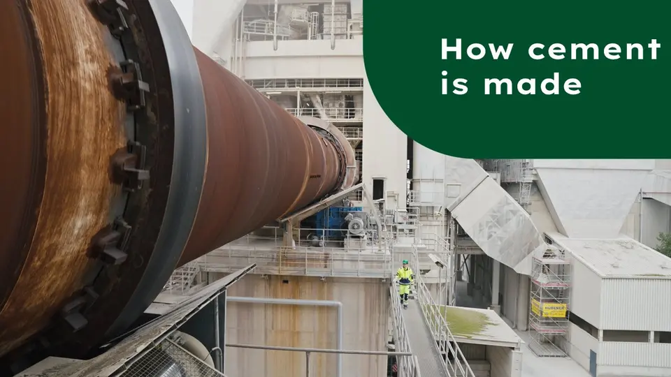 View of a cement works, on the left a rotary kiln, below on a railing a worker in protective clothing with a green helmet; at the top right "How cement is made" is written on a green background