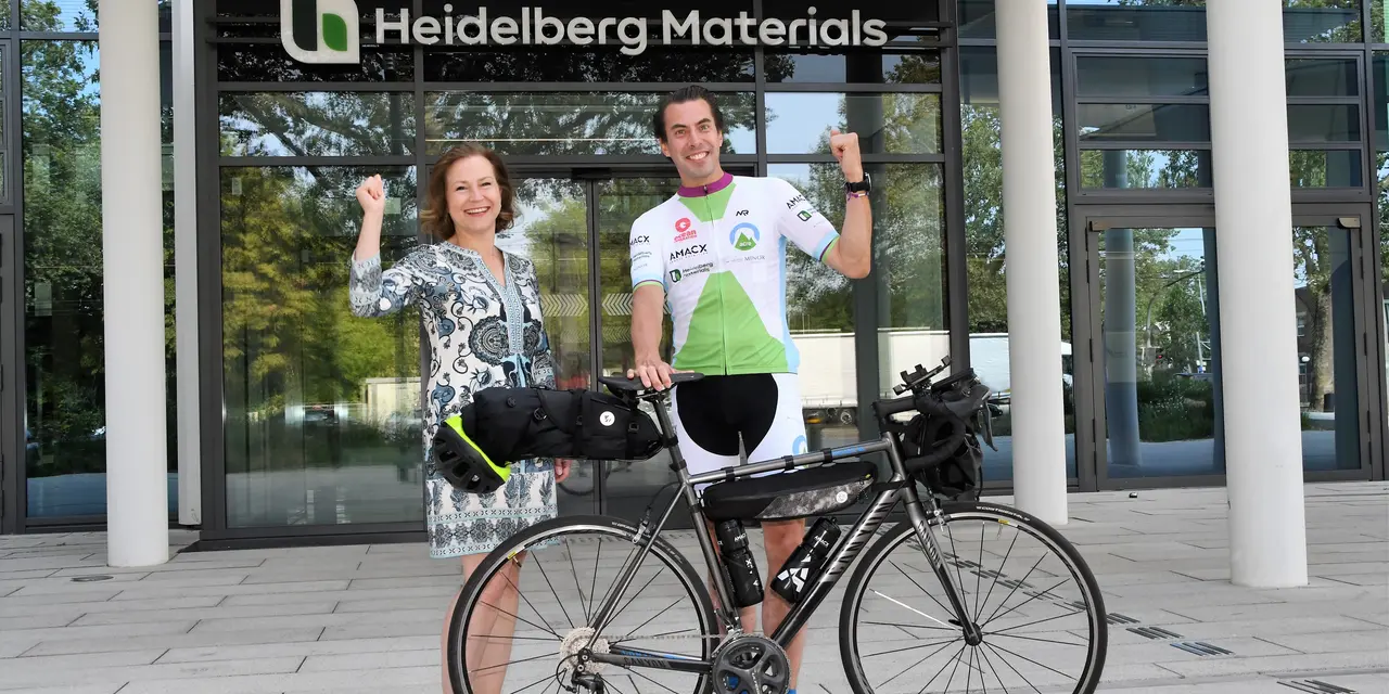 A man with a bicycle stands together with a woman in front of the Heidelberg Materials headquarters