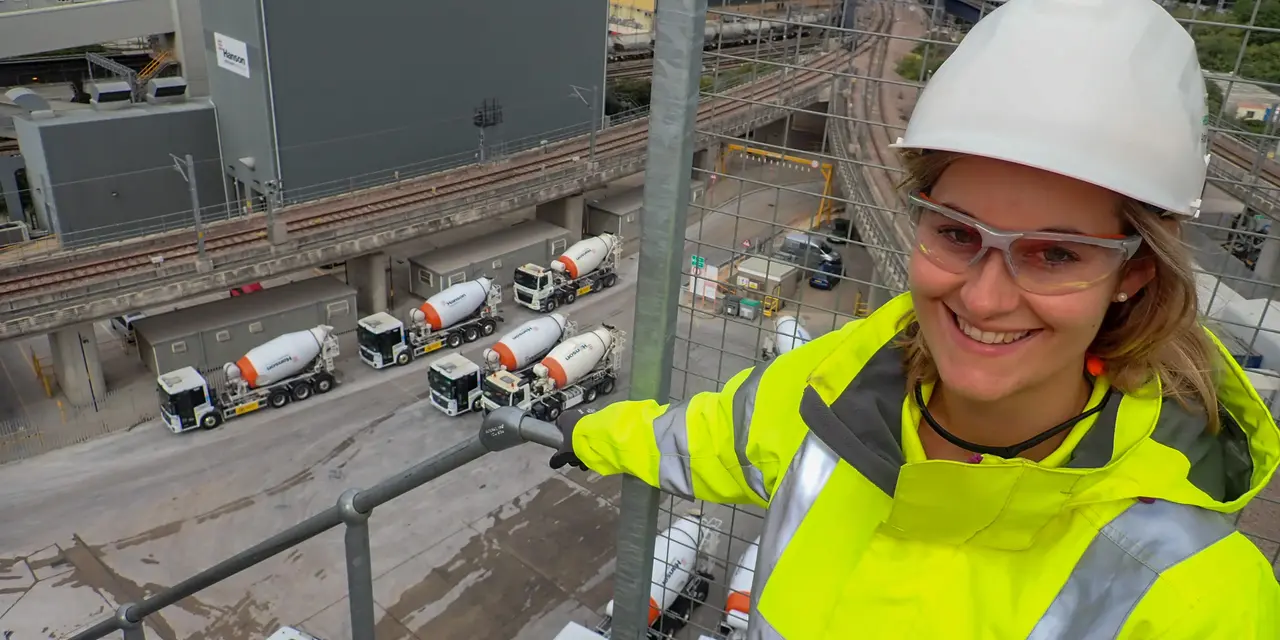 Woman with construction helmet standing on an industrial plant, concrete mixer trucks below