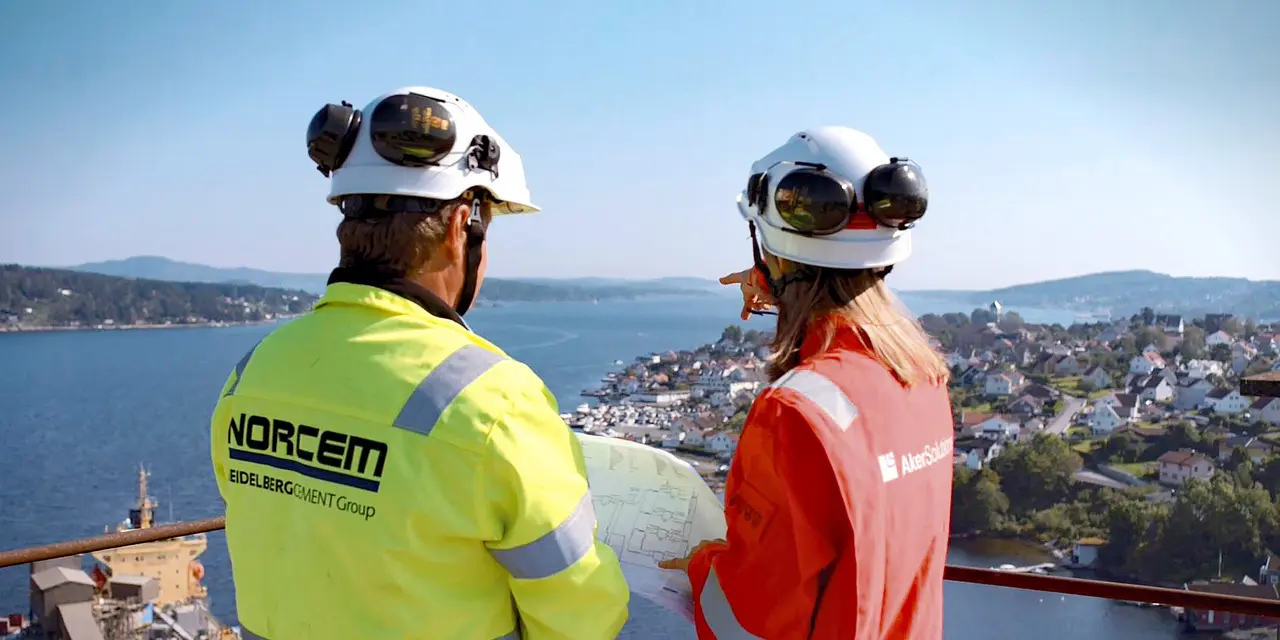 Two Heidelberg Materials employees are looking into the far, one of them is pointing at the ocean