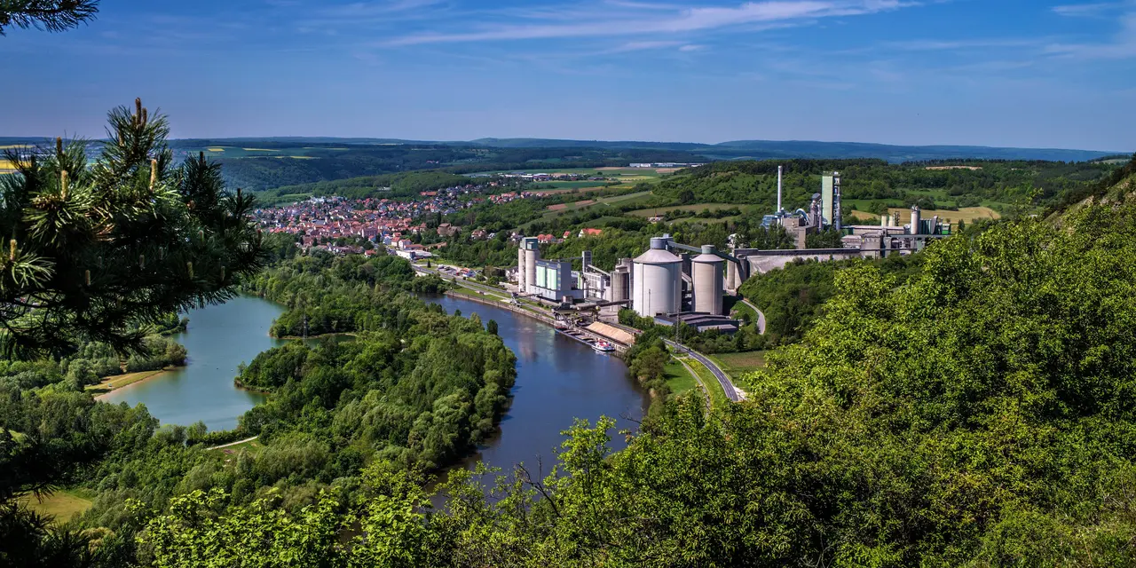 Blick von einem Hügel auf ein Zementwerk auf dem Lande neben einem Gewässer