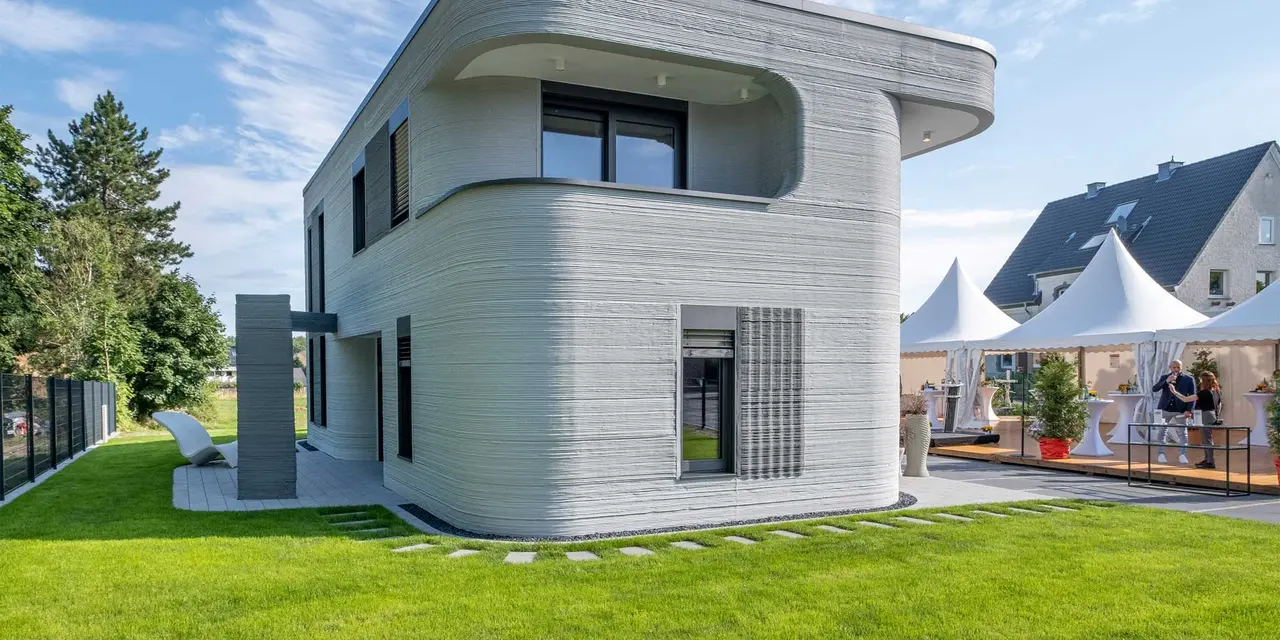 Modern two-story house with curved design and textured exterior, set on manicured lawn under blue sky