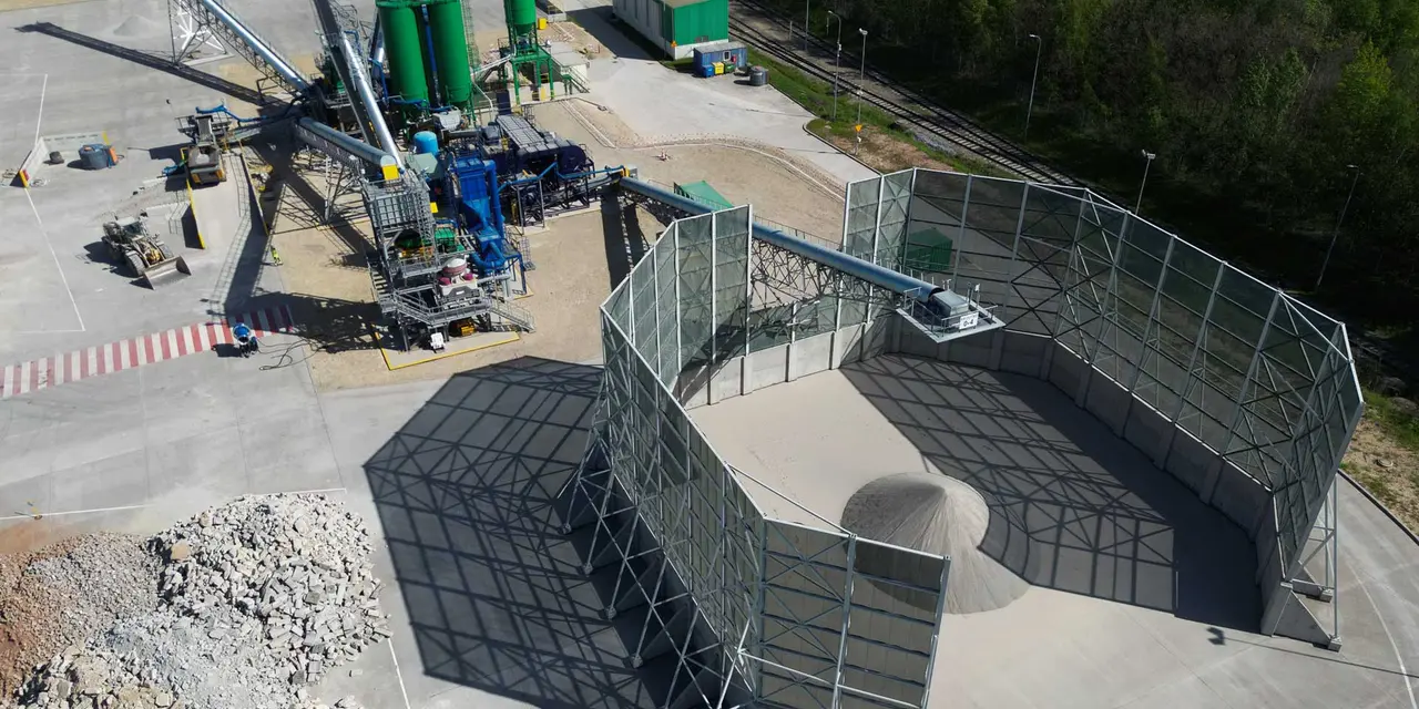 Industrial site with aggregate storage bins, conveyor systems, and silos.