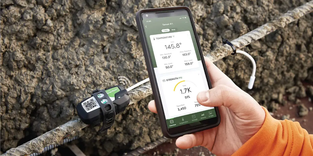 Eine Person, die ein Smartphone verwendet, um Baudaten zu überwachen. Der Telefonbildschirm zeigt Temperatur- und Festigkeitsmessungen. Unterhalb ist eine Sonde im Beton mit QR-Aufdruck.