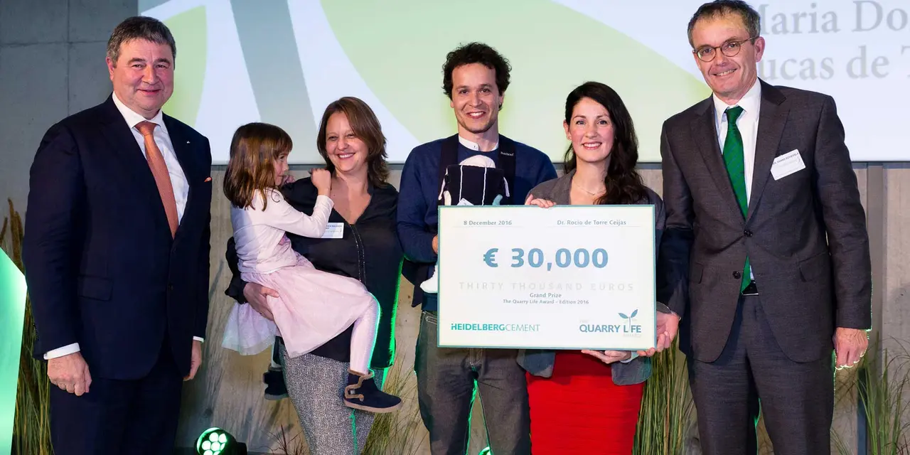 Sieben Personen auf einer Bühne, eines davon ist ein Kind auf dem Arm, eines ein Baby in einer Trage. Eine Person hält einen symbolischen Scheck mit dem Aufdruck 30.000 €, HeidelbergCement und Quarry Life Award.