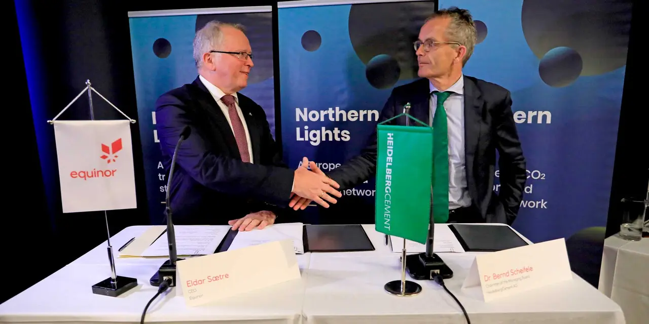 Zwei Führungskräfte geben sich bei einer Unterzeichnungszeremonie die Hand mit Bannern des ‘Northern Lights’ Projekts im Hintergrund, die auf die Beteiligung von Equinor, Shell und Total hinweisen.
