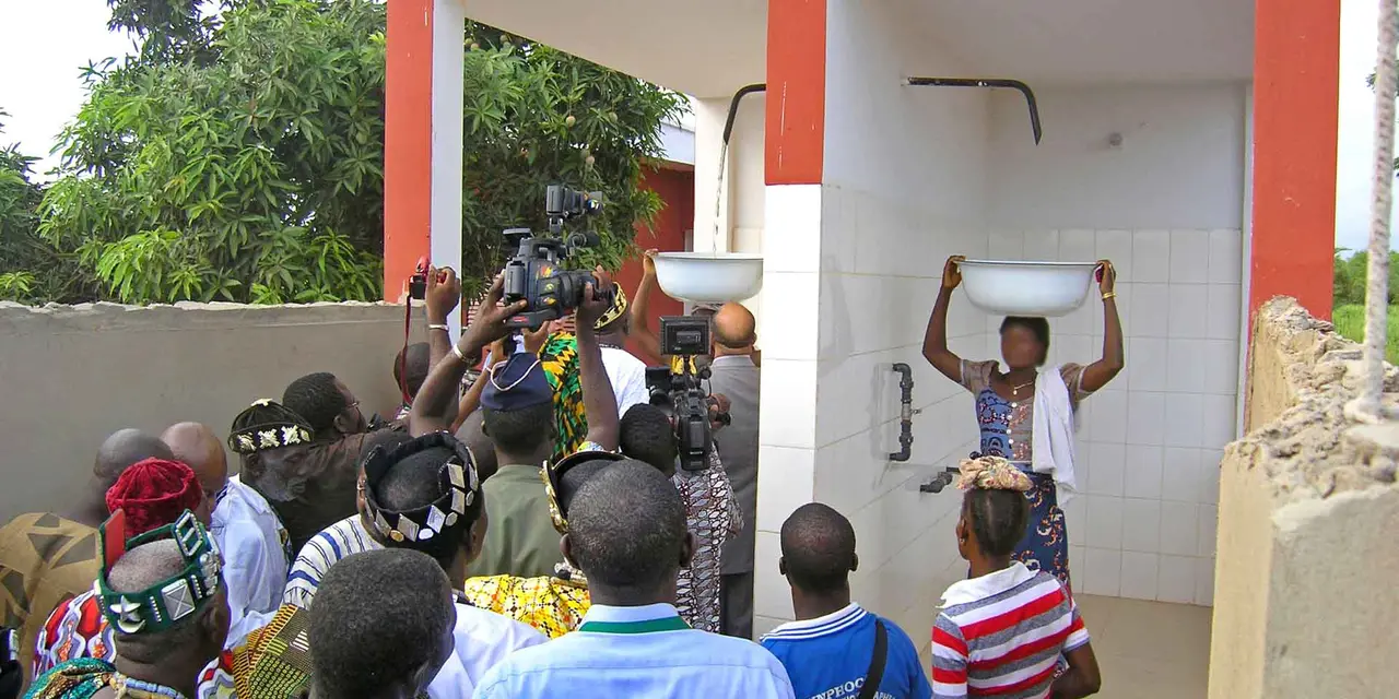 A group of people at a water pump station with a sign in French indicating the foundation’s involvement and operating hours.